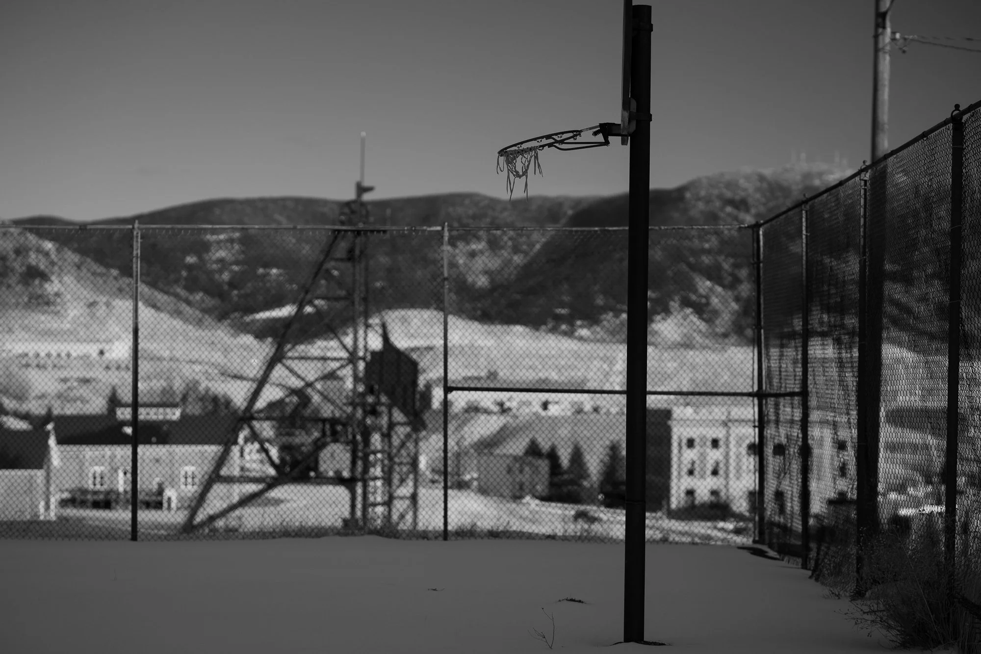Snow-covered outdoor basketball court with a weathered hoop and town in the background