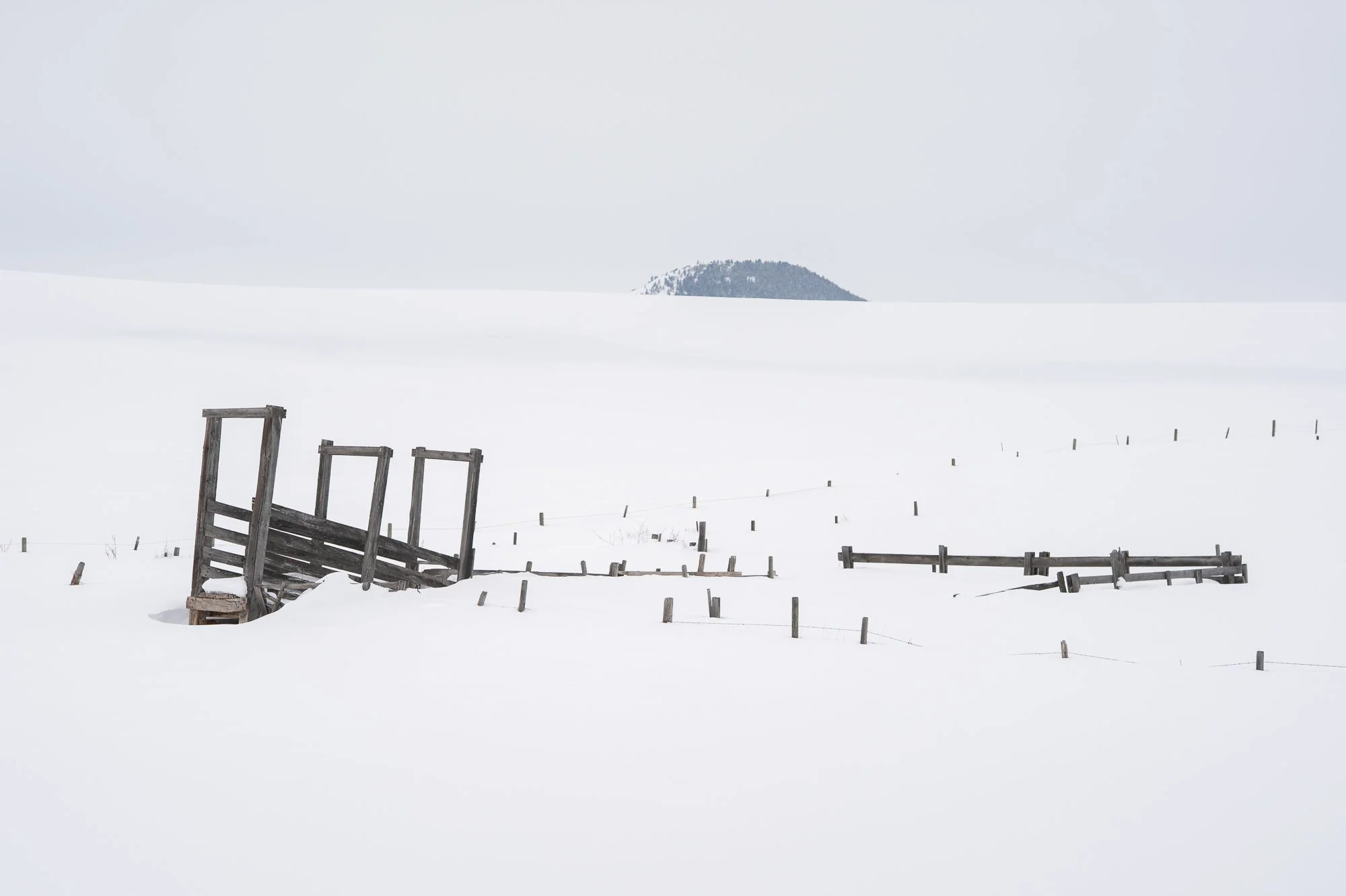 Minimal snow covered ranch landscape with old wooden fence and distant hill
