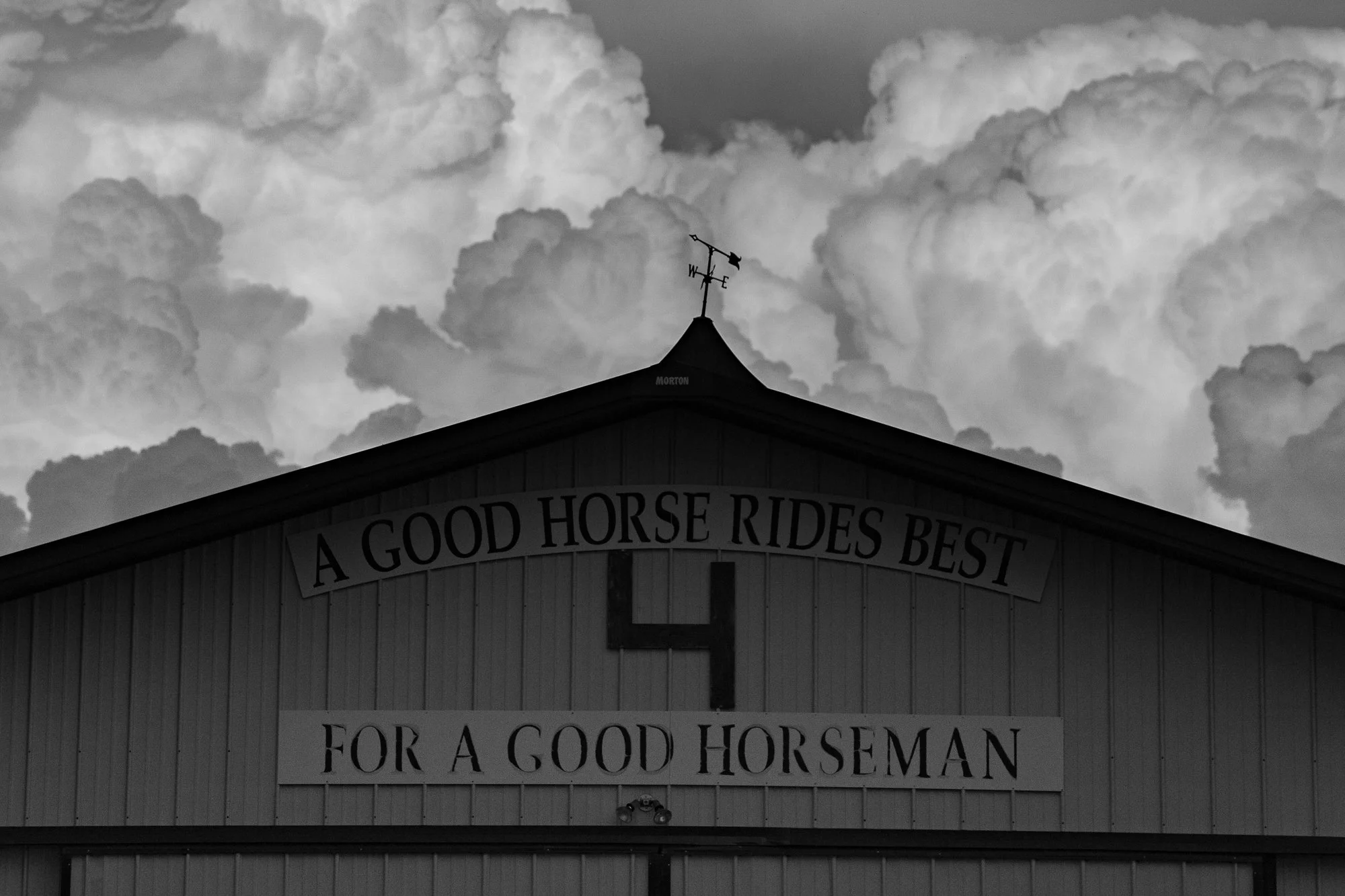 Barn at Haythorn Ranch in Nebraska with the phrase “A Good Horse Rides Best for a Good Horseman” beneath dramatic clouds in the Sandhills sky.