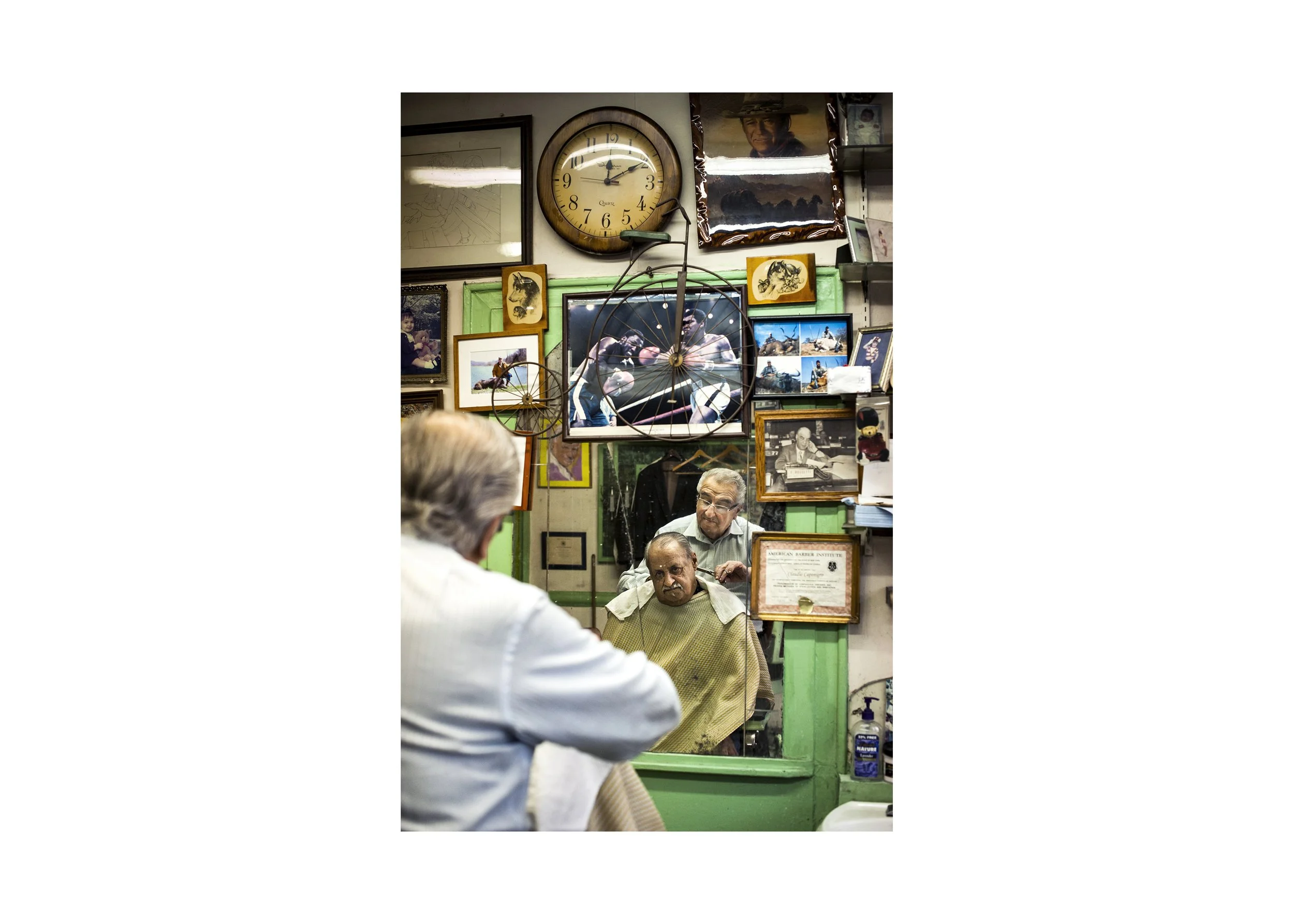 Barber and customer reflected in a worn mirror inside a cluttered, character-rich barbershop with vintage photographs and décor.