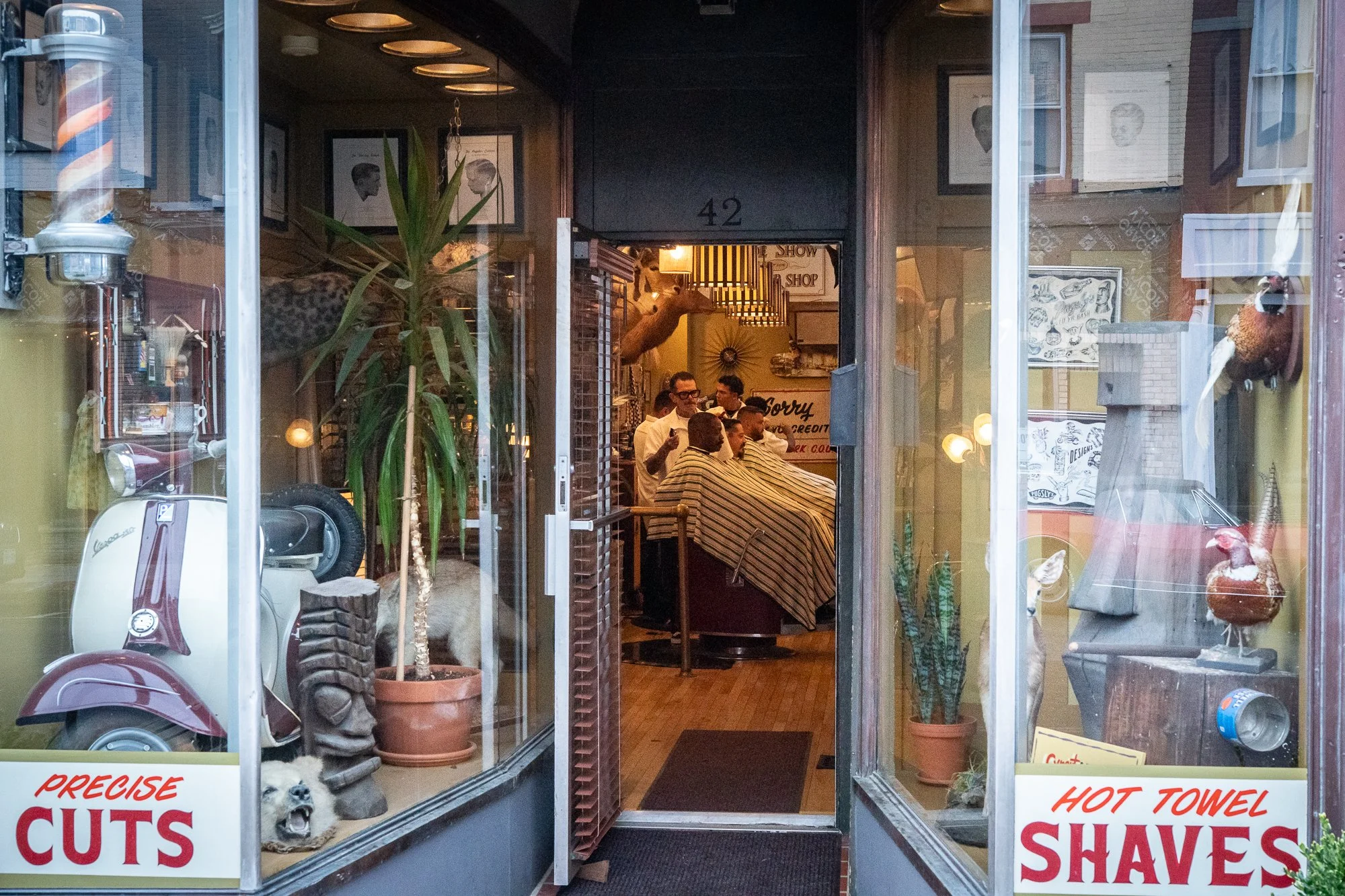 Barbers and clients inside Pugsly’s Barbershop in Kingston, New York, viewed through the front entrance.
