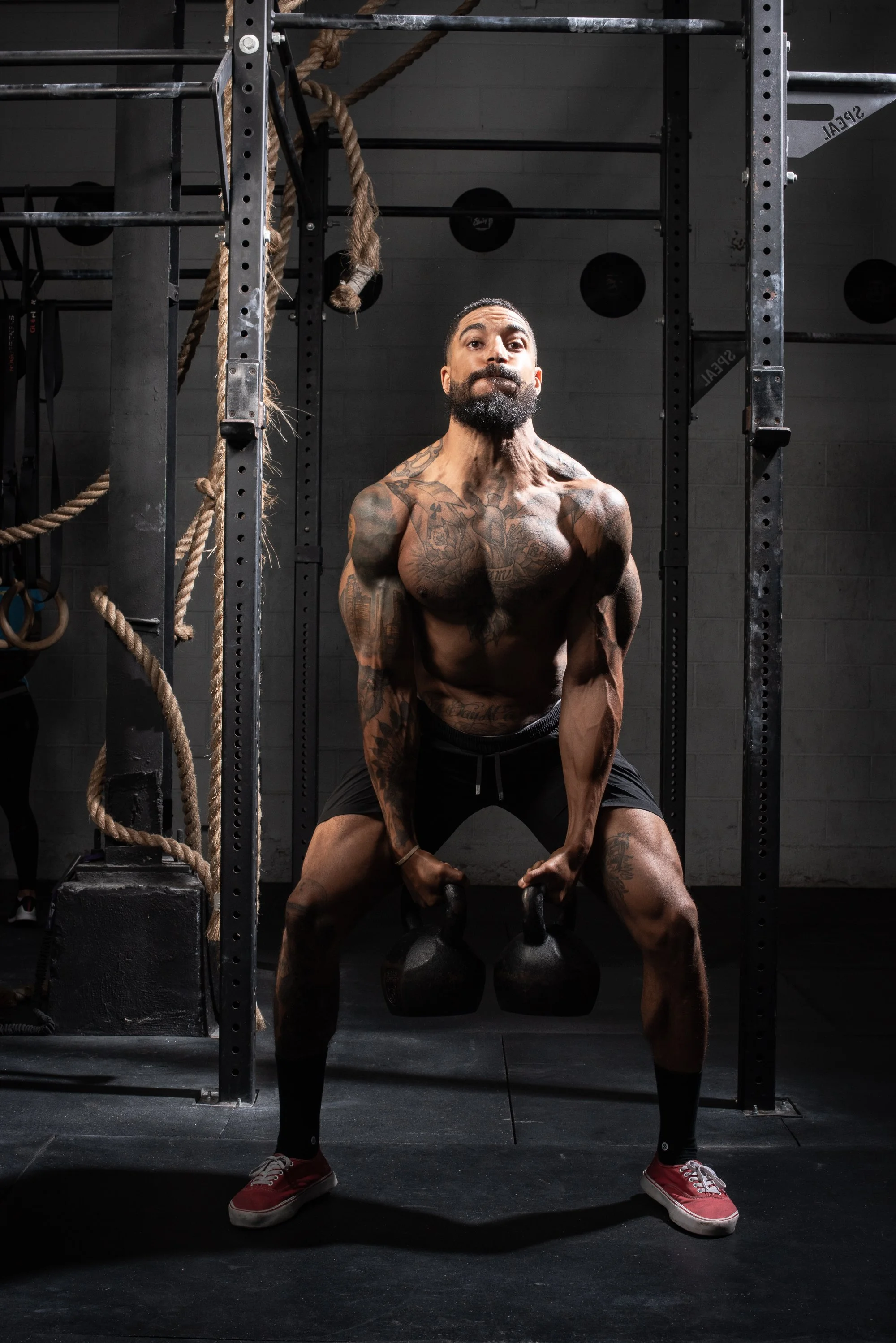 Athlete lifts two kettlebells from a low position in a Colorado gym, showing visible strain