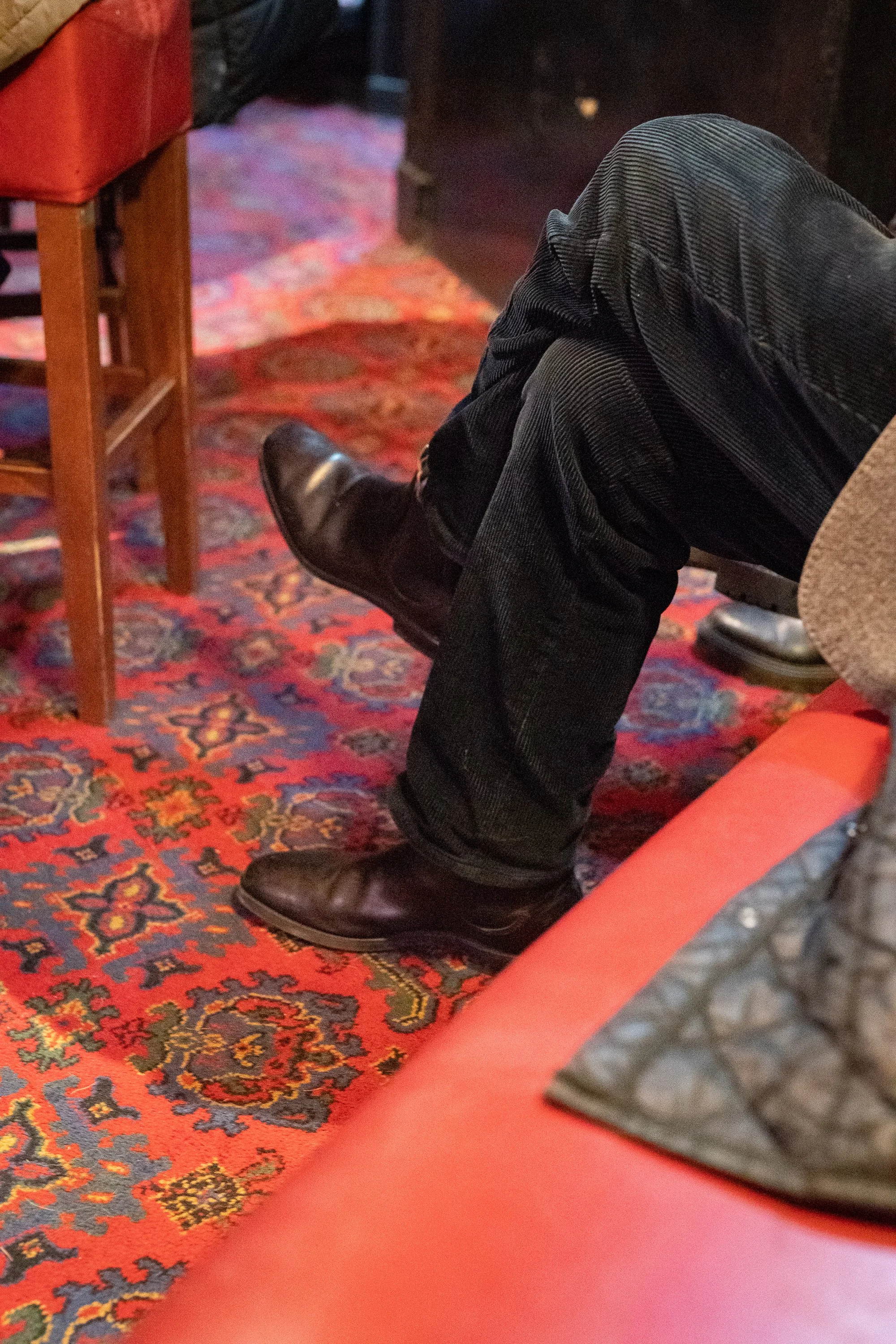 Close-up of boots resting on red patterned carpet inside traditional pub