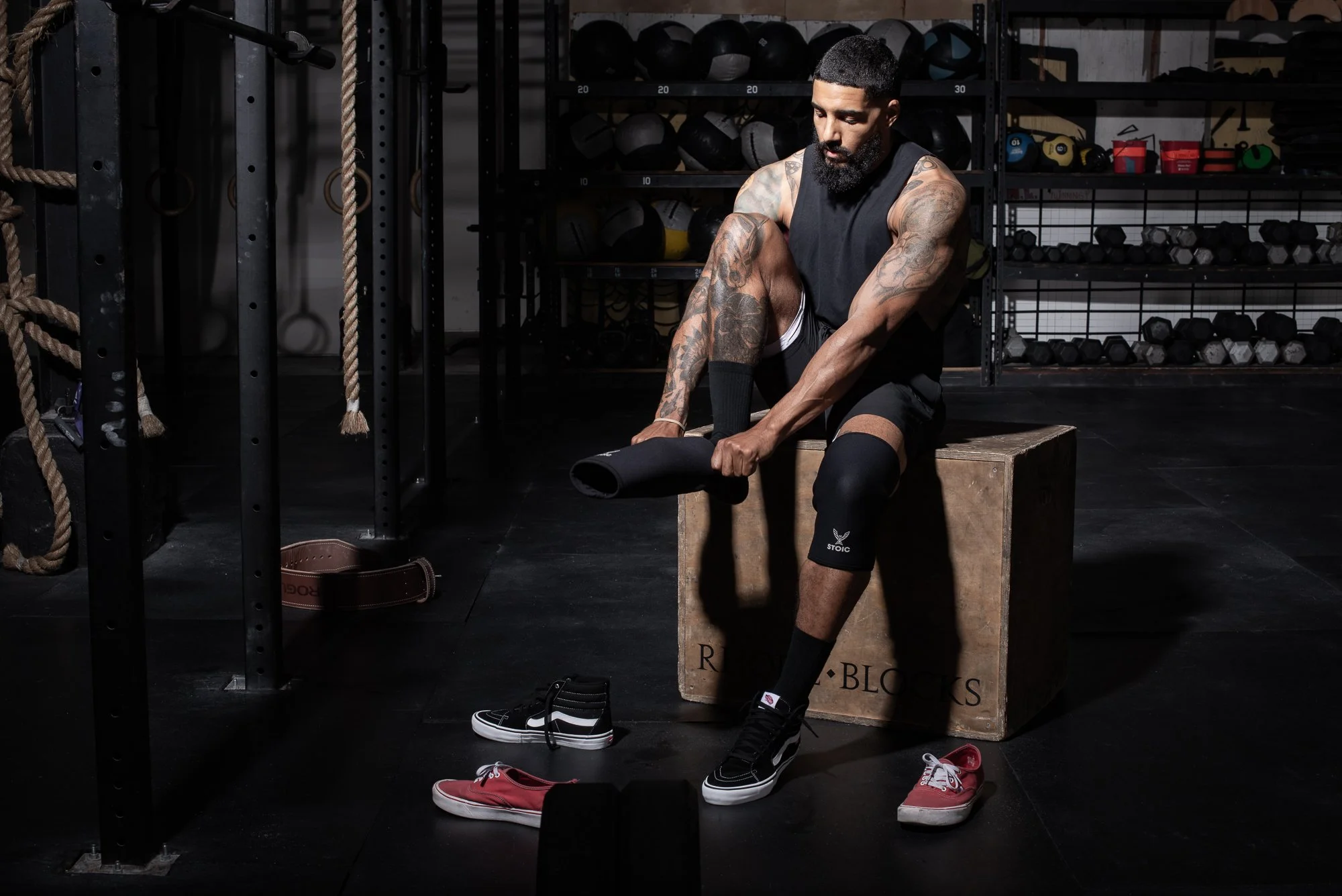 Athlete sits on a wooden box in a Colorado gym changing shoes, with training equipment and  weights around him