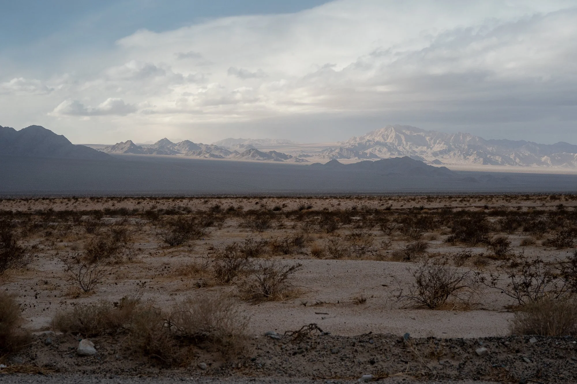 California desert landscape with scrub brush, distant mountains, and heavy clouds