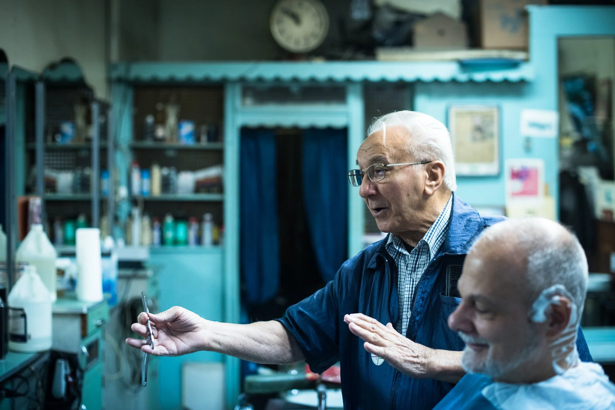 An elderly barber laughs with his client inside Tony’s Barbershop in Brooklyn, New York.