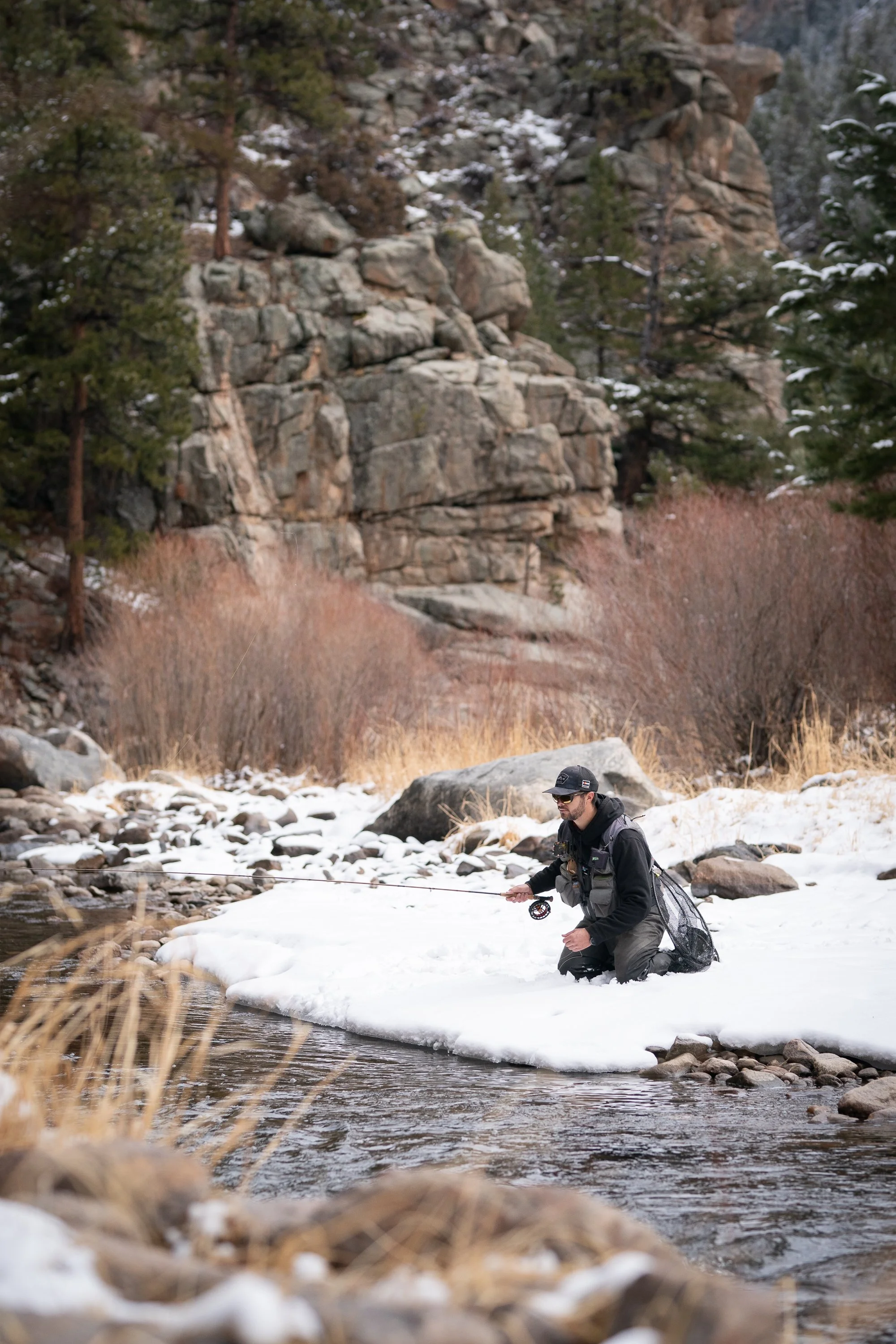 A fly fisherman casting into a winter stream in a rocky canyon near Estes Park, CO