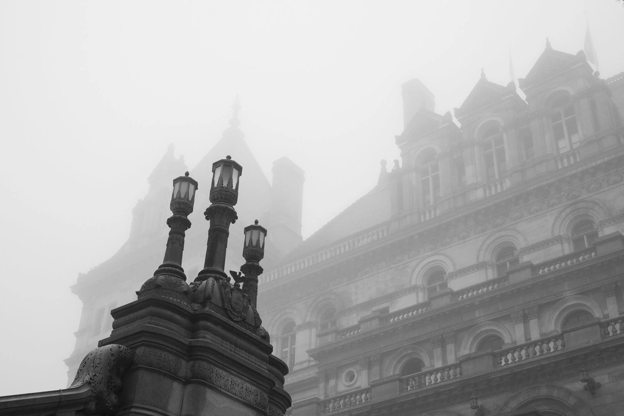 Black and white photograph of stone balustrades and historic lanterns at the New York State Capitol in fog, Albany