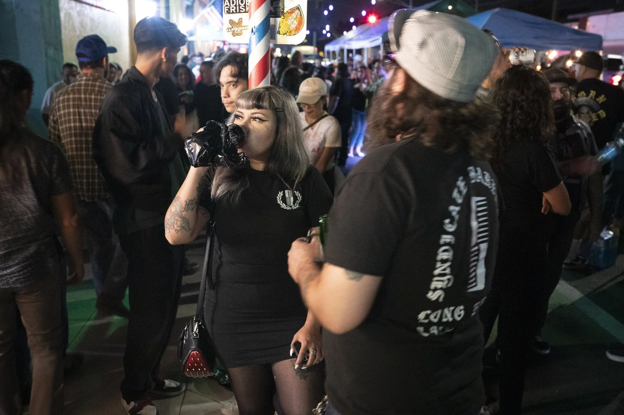 Groups of people standing and talking on a crowded Long Beach street at night during a barbershop event