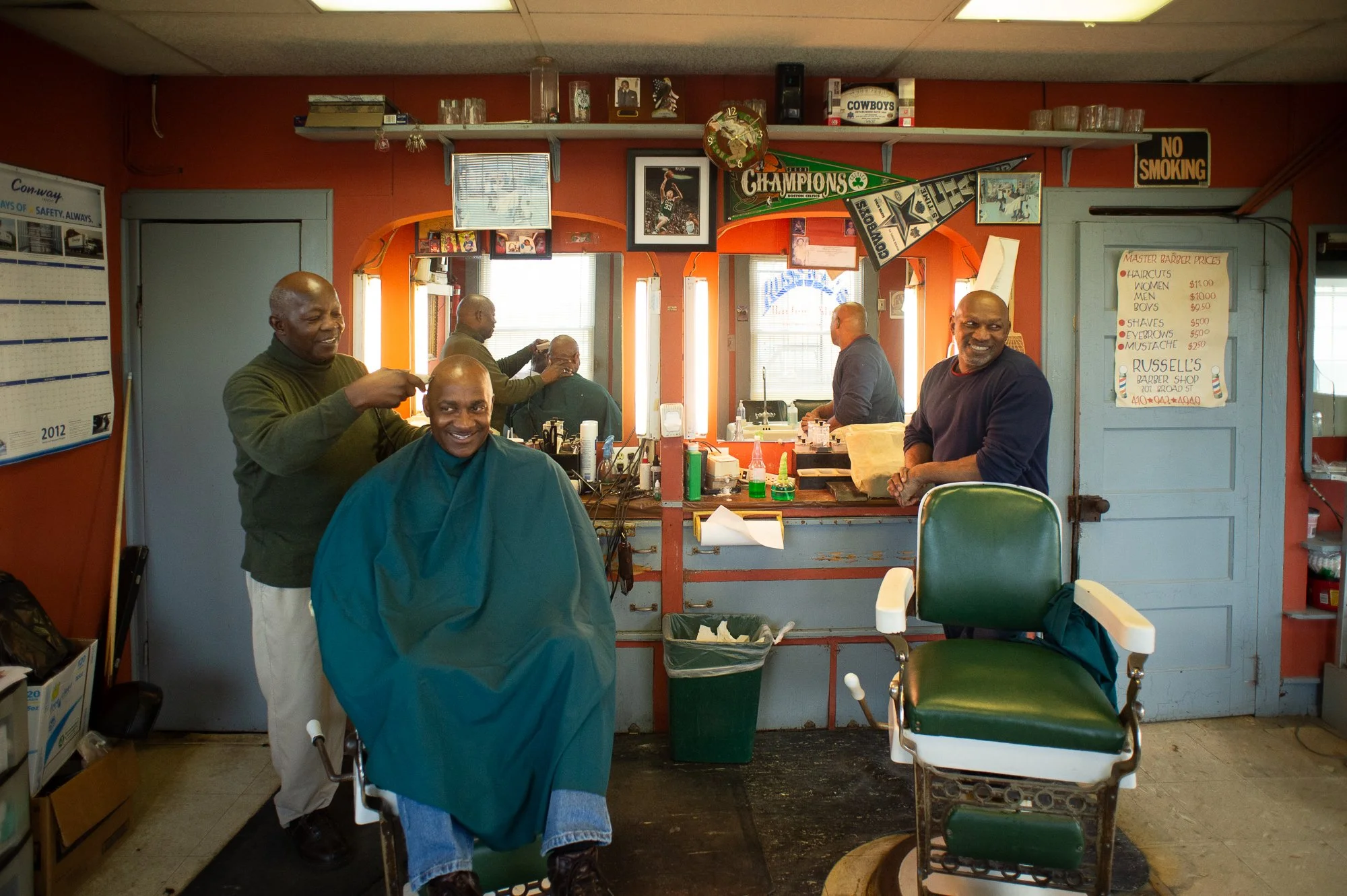 Barber cutting hair while other men watch and talk inside a lively Black barbershop