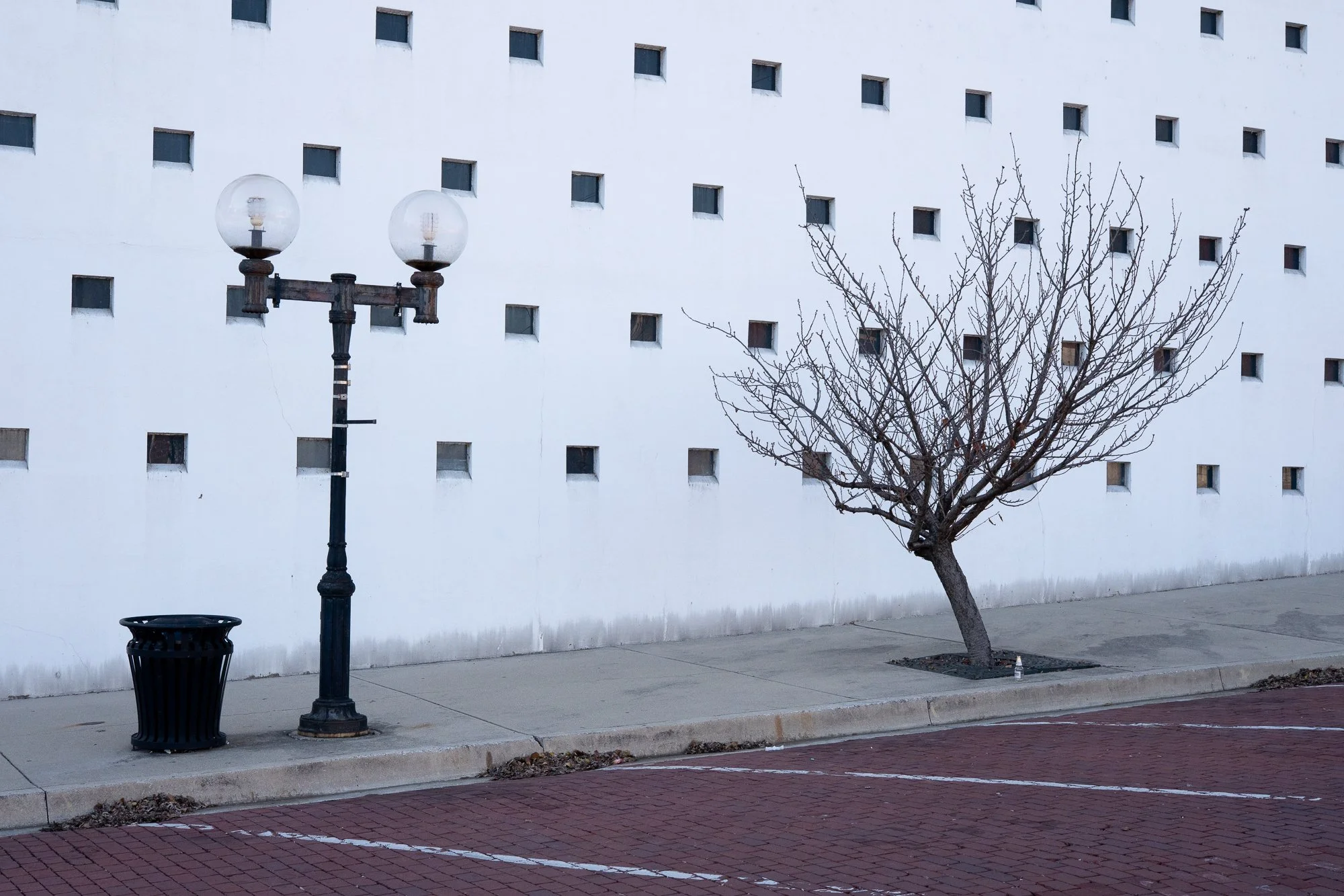 Small tree and streetlamp against a white wall with square openings in Alton, Illinois