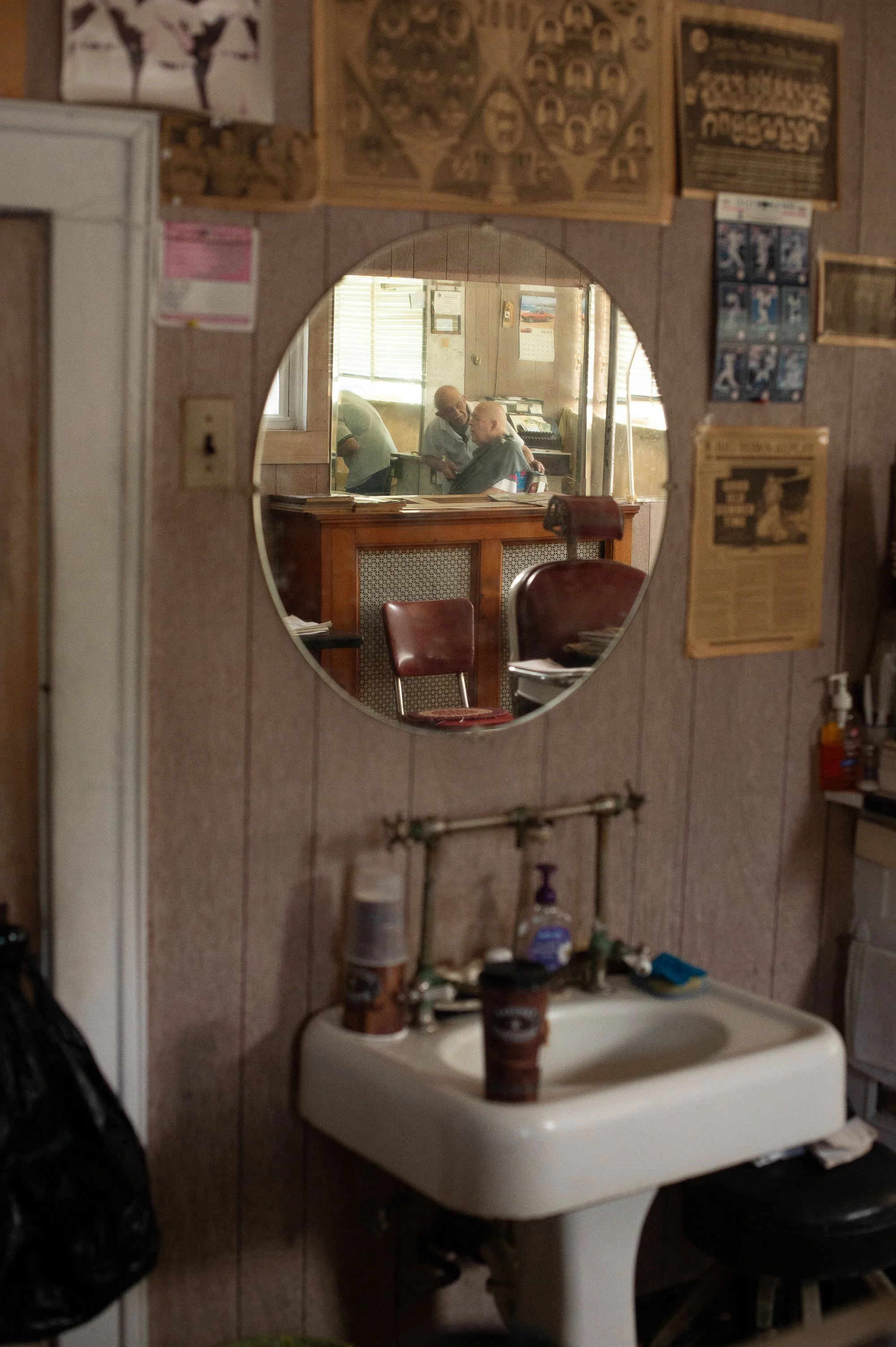 mirror reflection of barber cutting hair inside Tony's Barbershop Greenwich Connecticut vintage interior