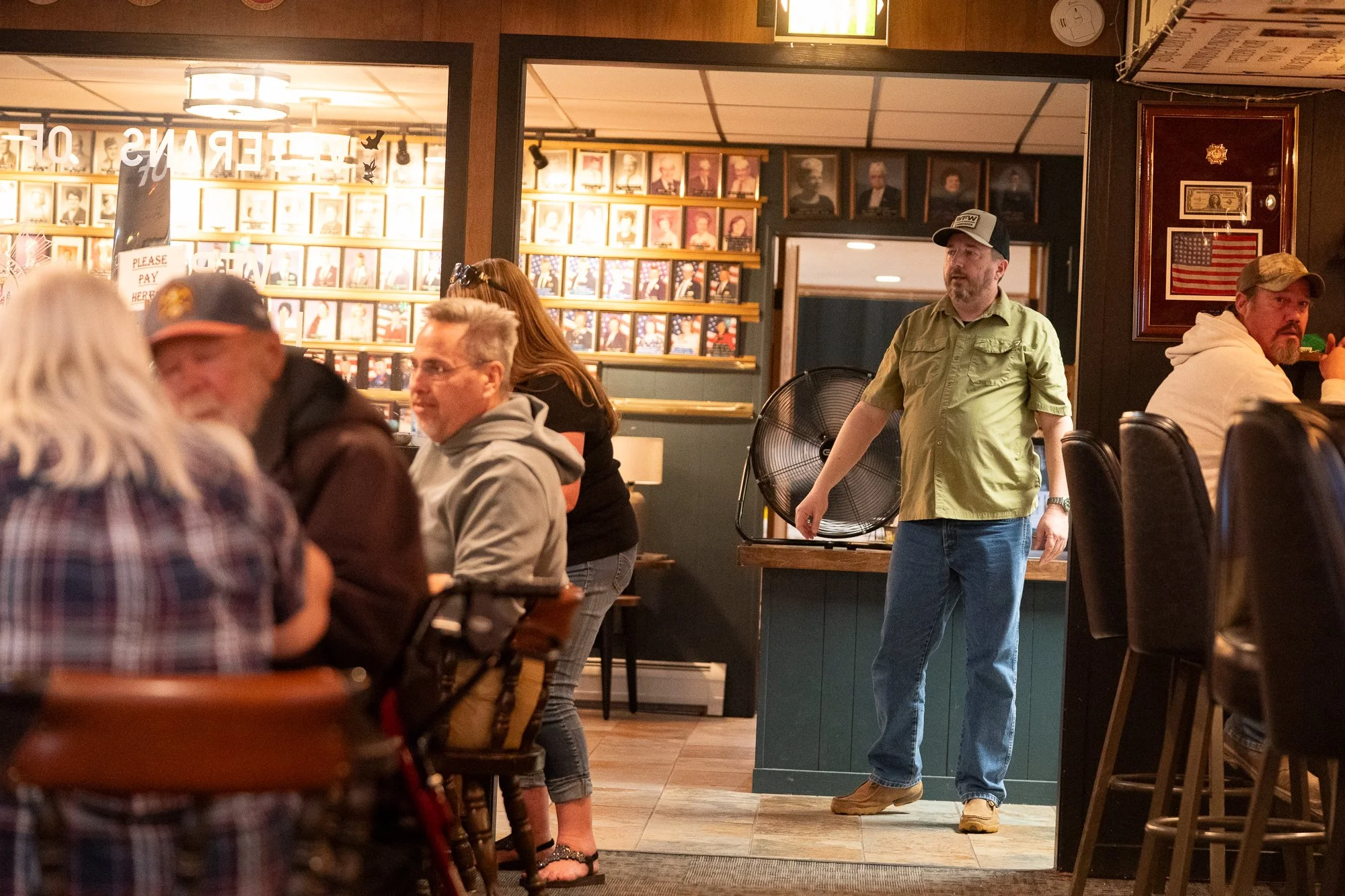 People gathered inside a VFW hall with portraits and military memorabilia on the walls