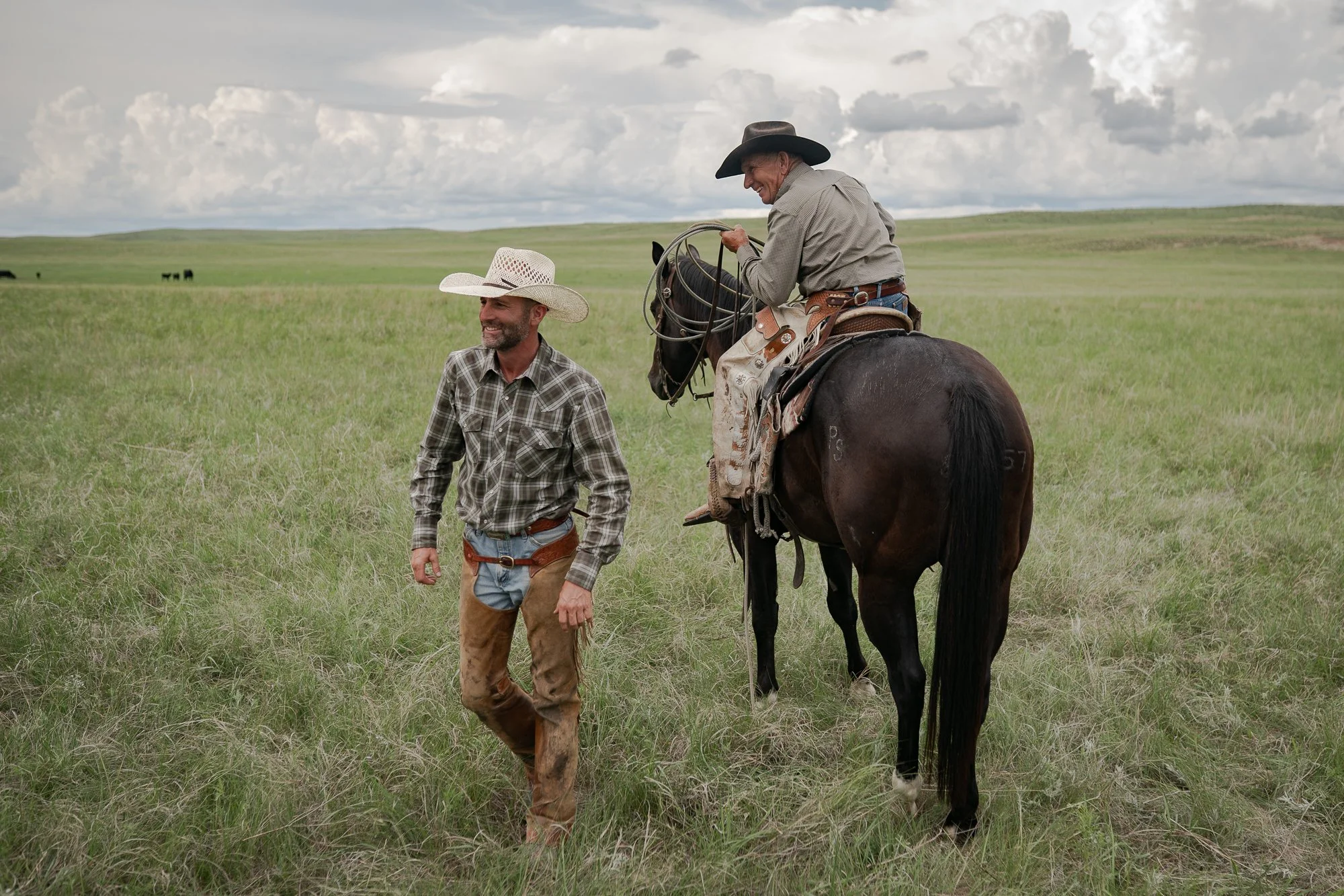 Two cowboys laughing together on the grasslands of the Nebraska Sandhills at Haythorn Ranch.
