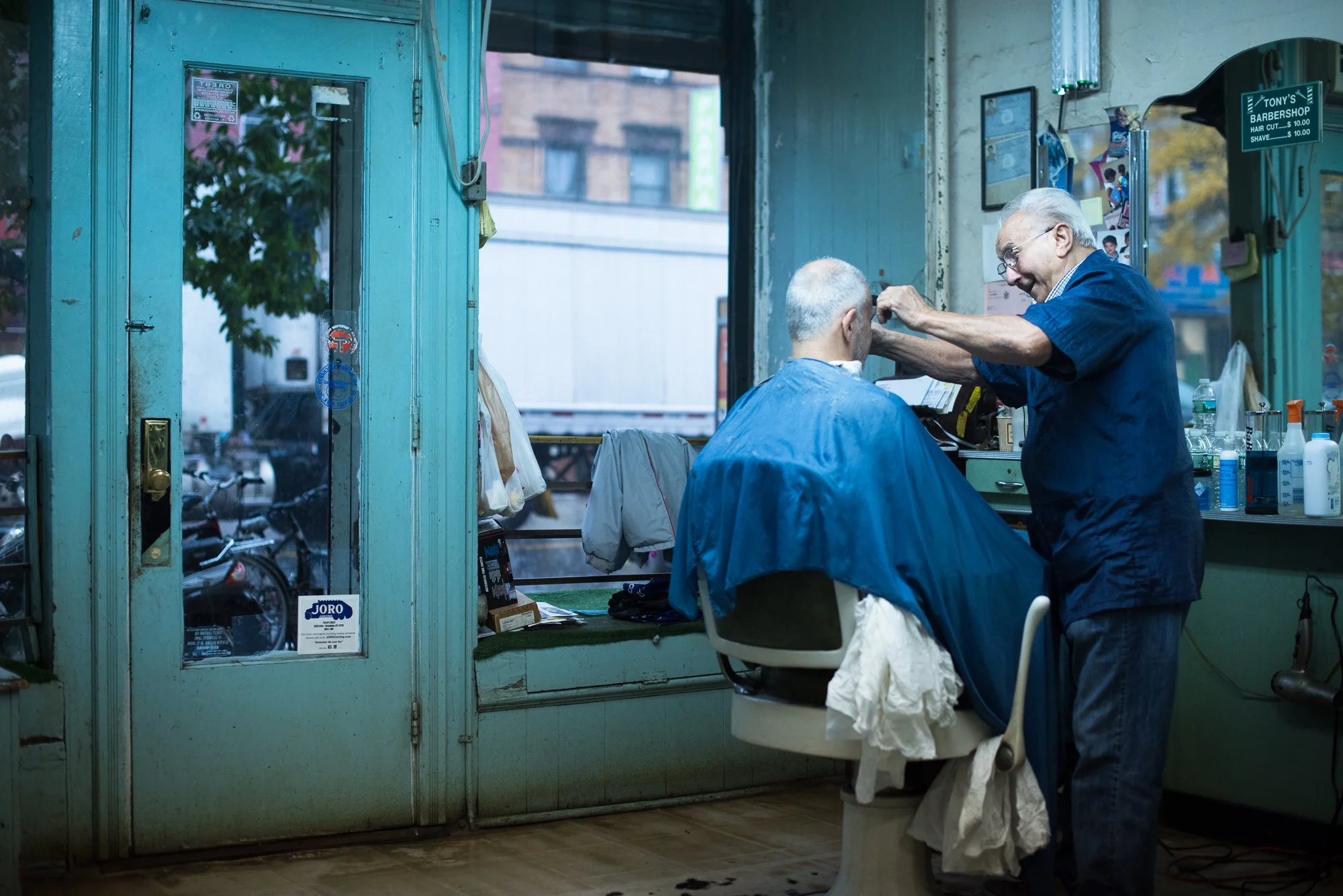 A barber cuts a client’s hair near the front window of Tony’s Barbershop in Brooklyn, New York.
