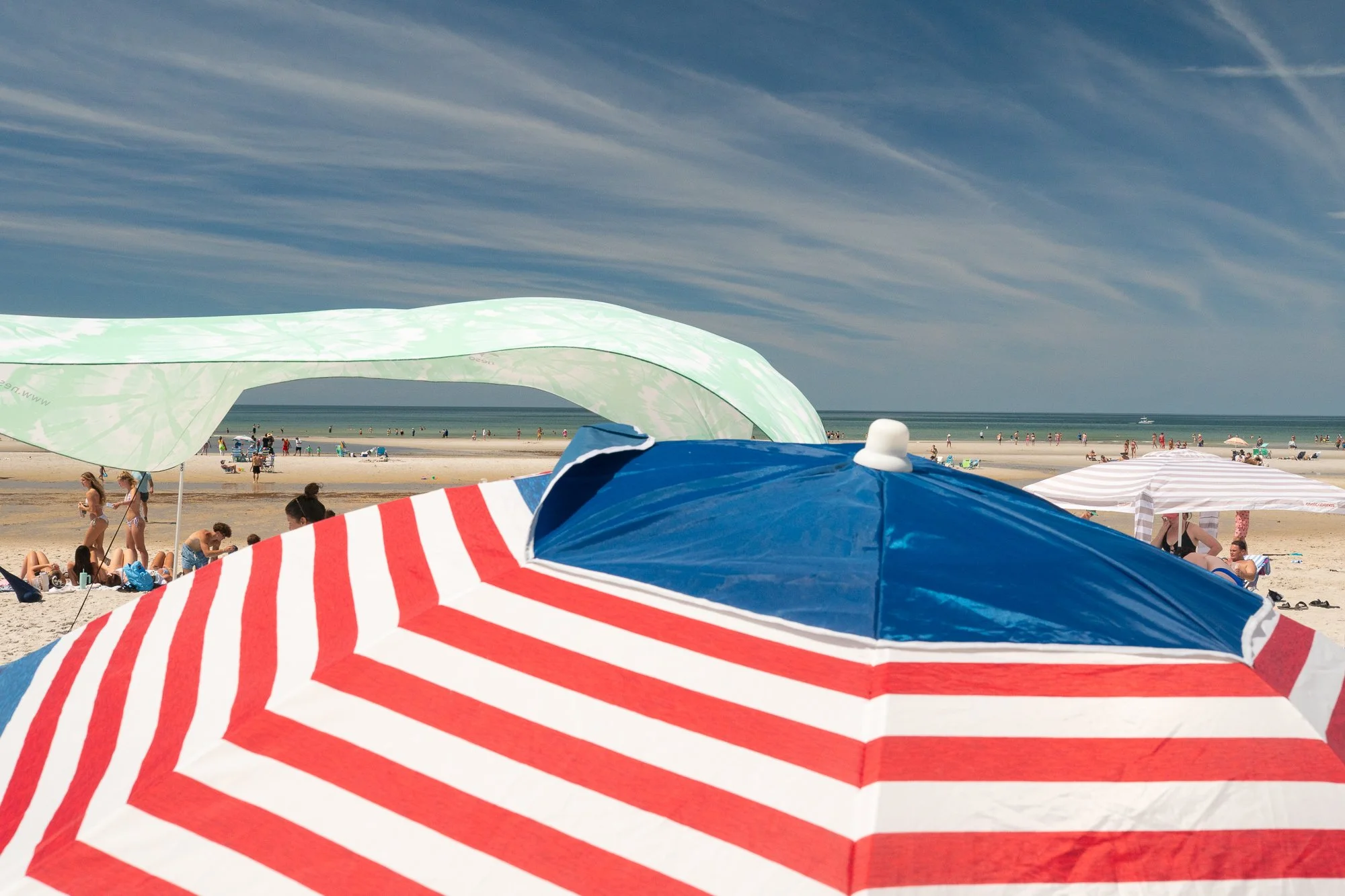 Colorful beach umbrellas on Cape Cod with people relaxing near the shoreline on a bright summer day