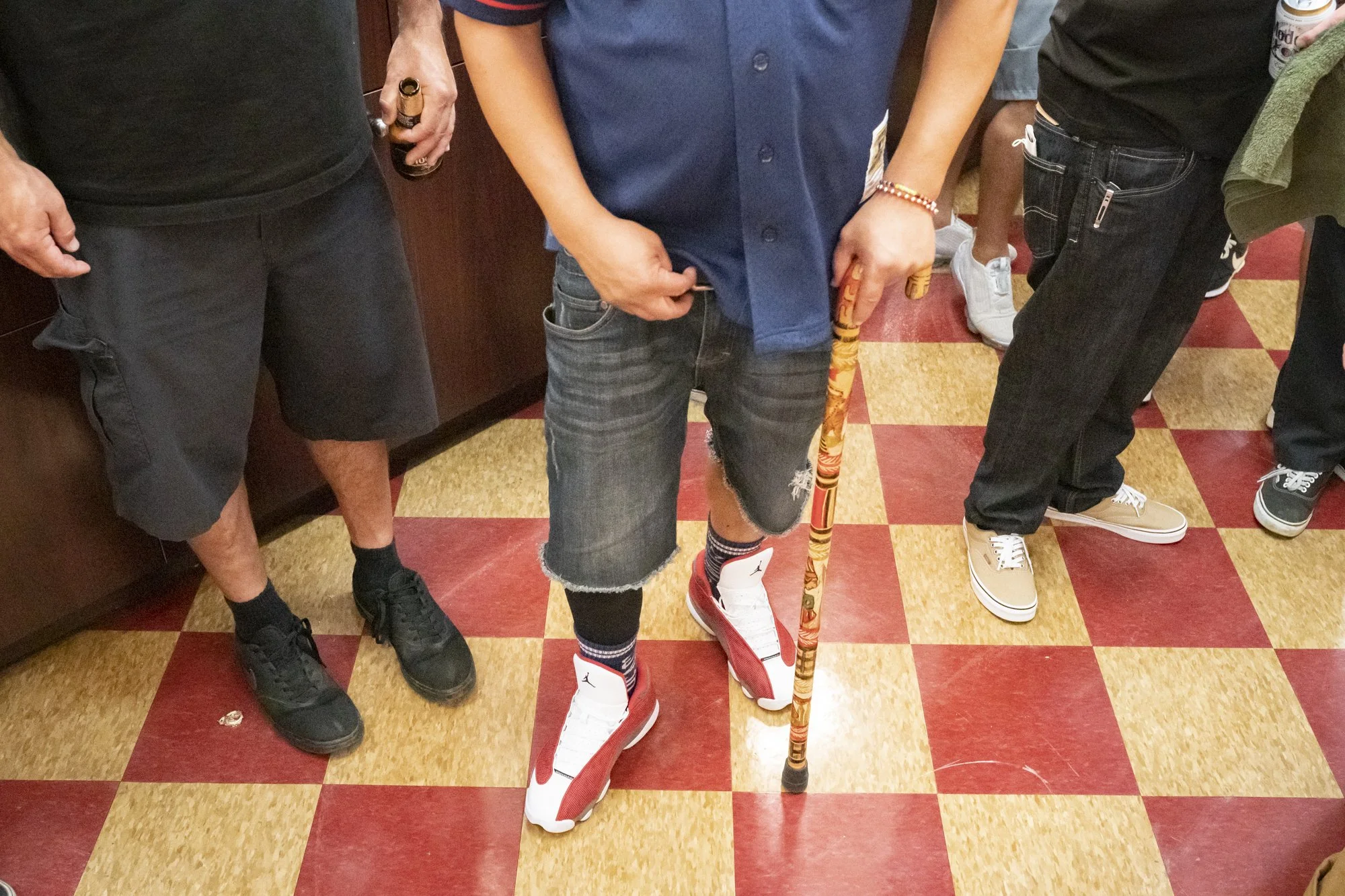 Detail shot of Air Jordan sneakers, a carved wooden cane, and Vans shoes on the red and cream checkerboard floor inside Syndicate Barbershop during the anniversary party