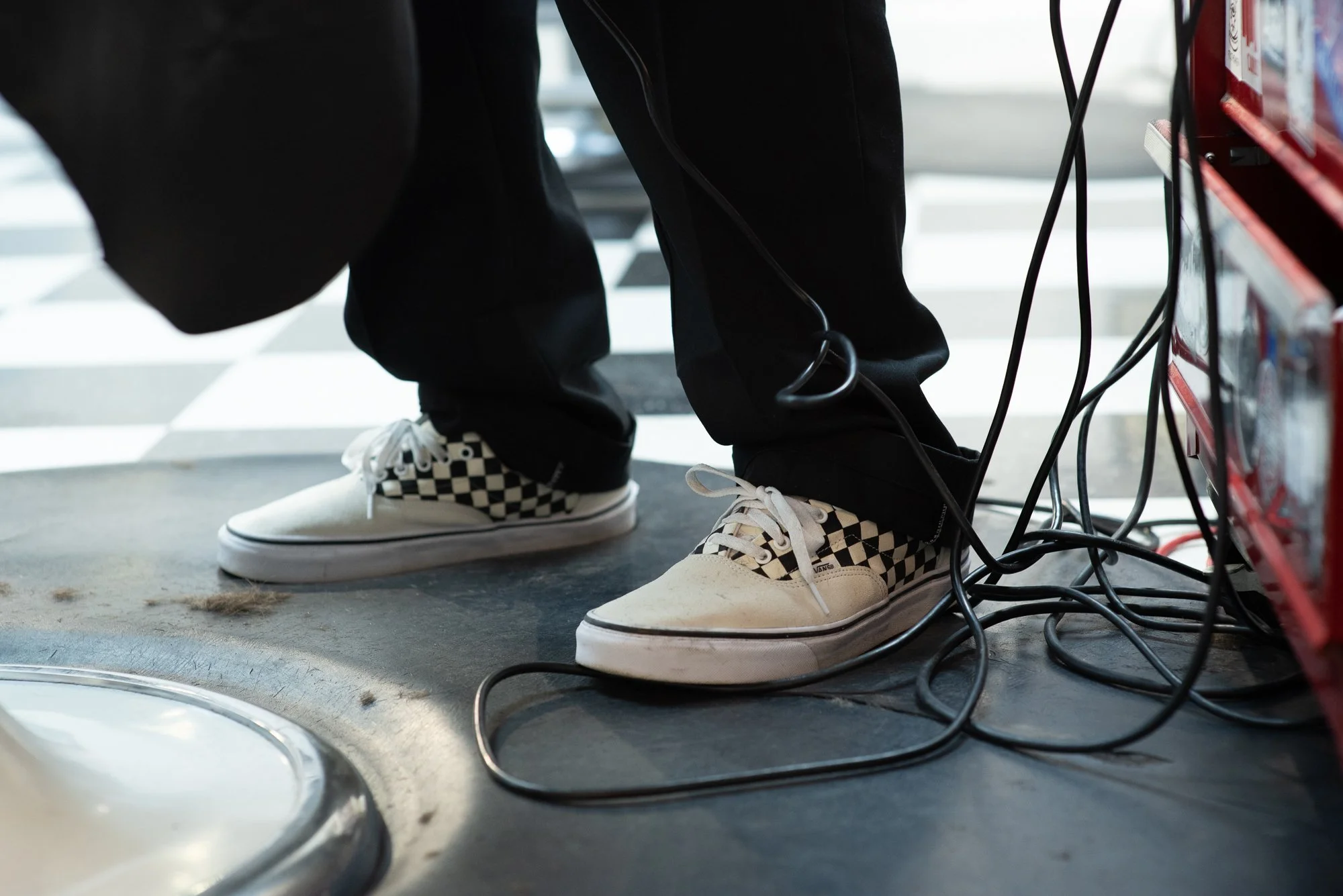 Checkerboard Vans shoes standing on barbershop floor with hair clippings and electrical cords
