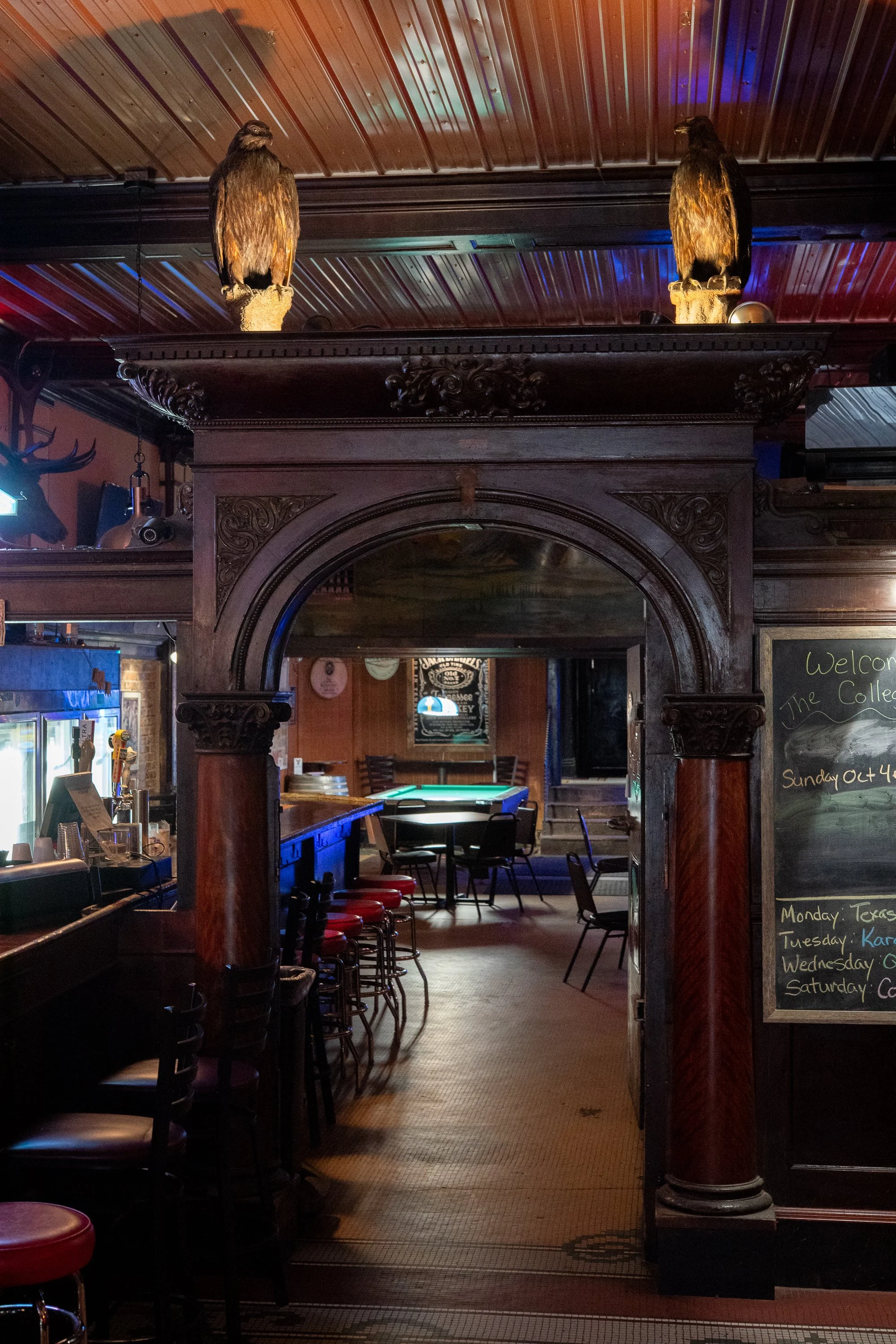 Ornate carved wooden archway and decorative columns inside the College Inn in Douglas, Wyoming, with mounted birds above the structure and a pool table in the back room.