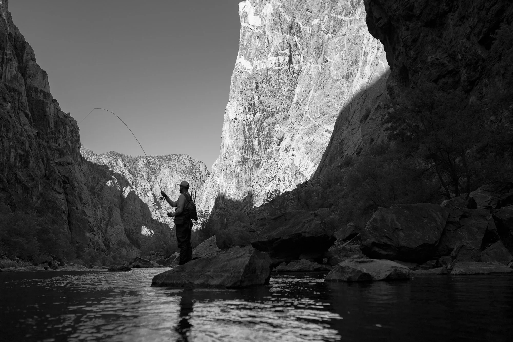 A fly angler stands in the river casting beneath towering canyon walls in Black Canyon