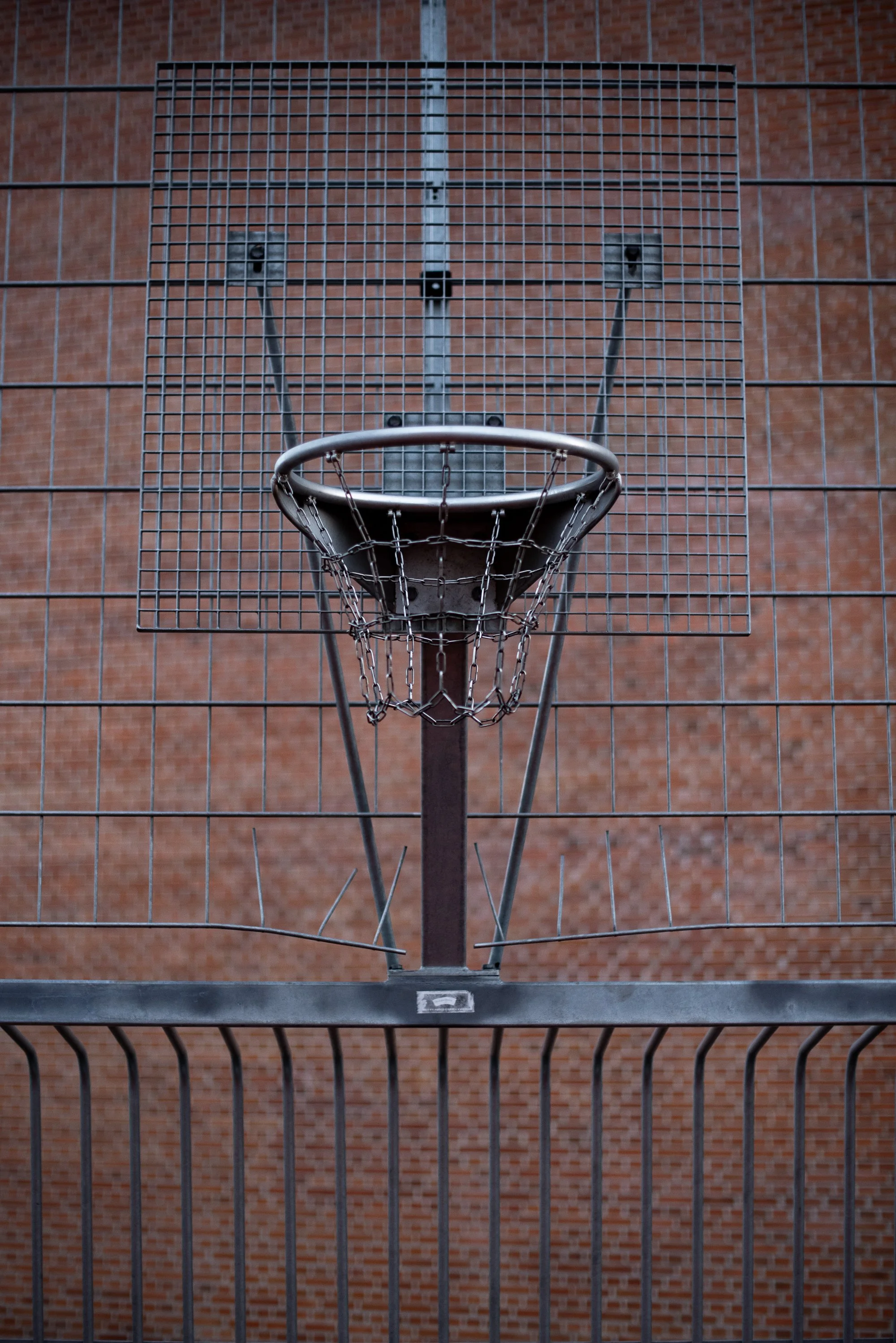 Chain-net basketball hoop mounted on a pole in front of a brick wall on a European outdoor court.