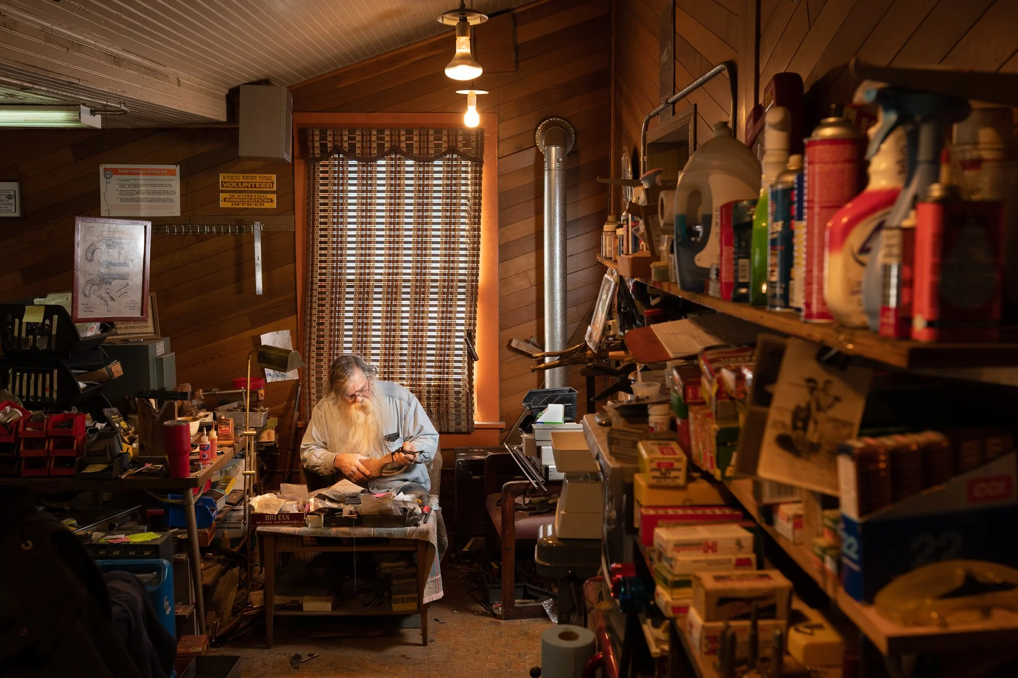 Man working on a rifle at a cluttered workbench in a Wyoming shop
