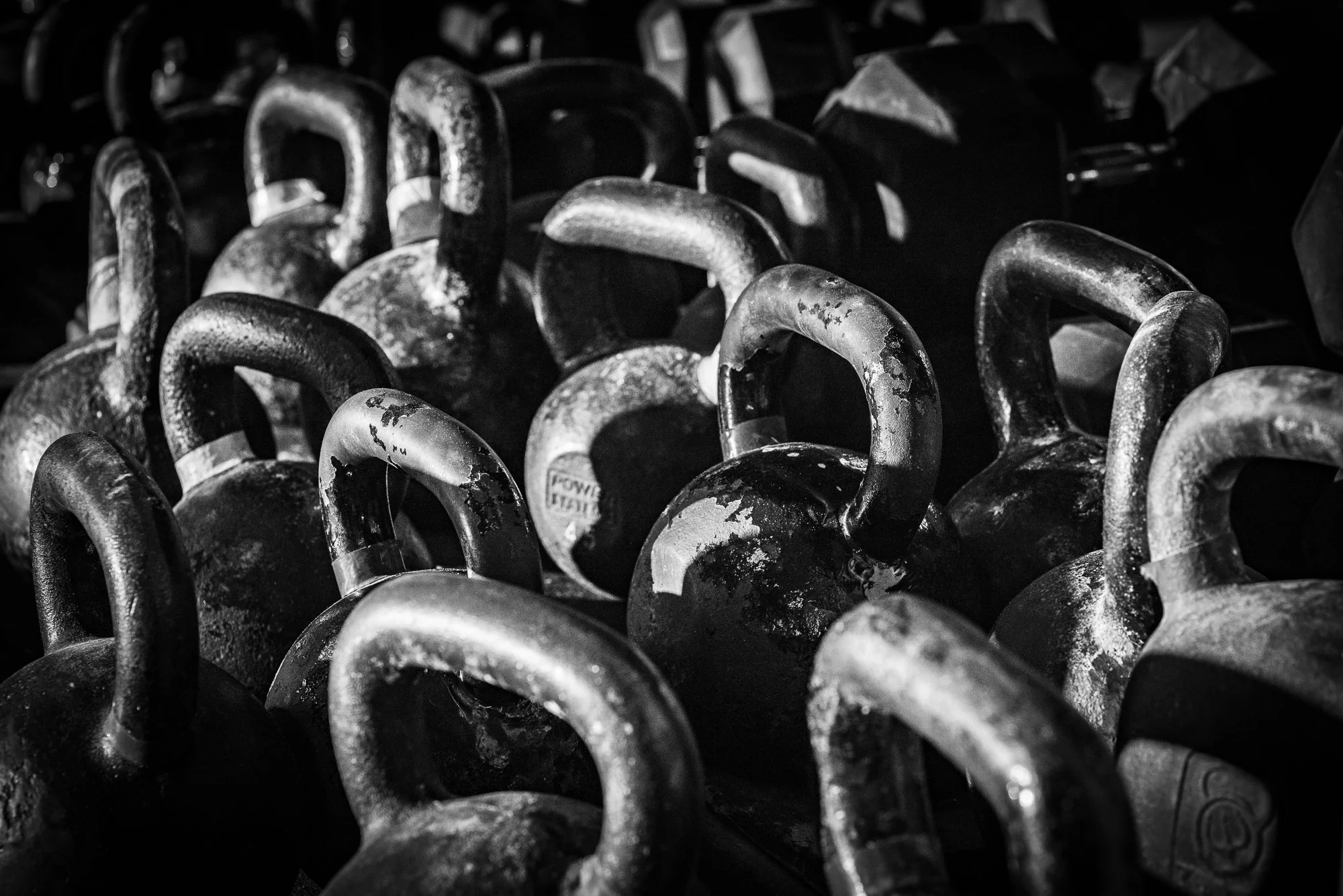 black and white kettlebells lined up in gym showing wear and texture