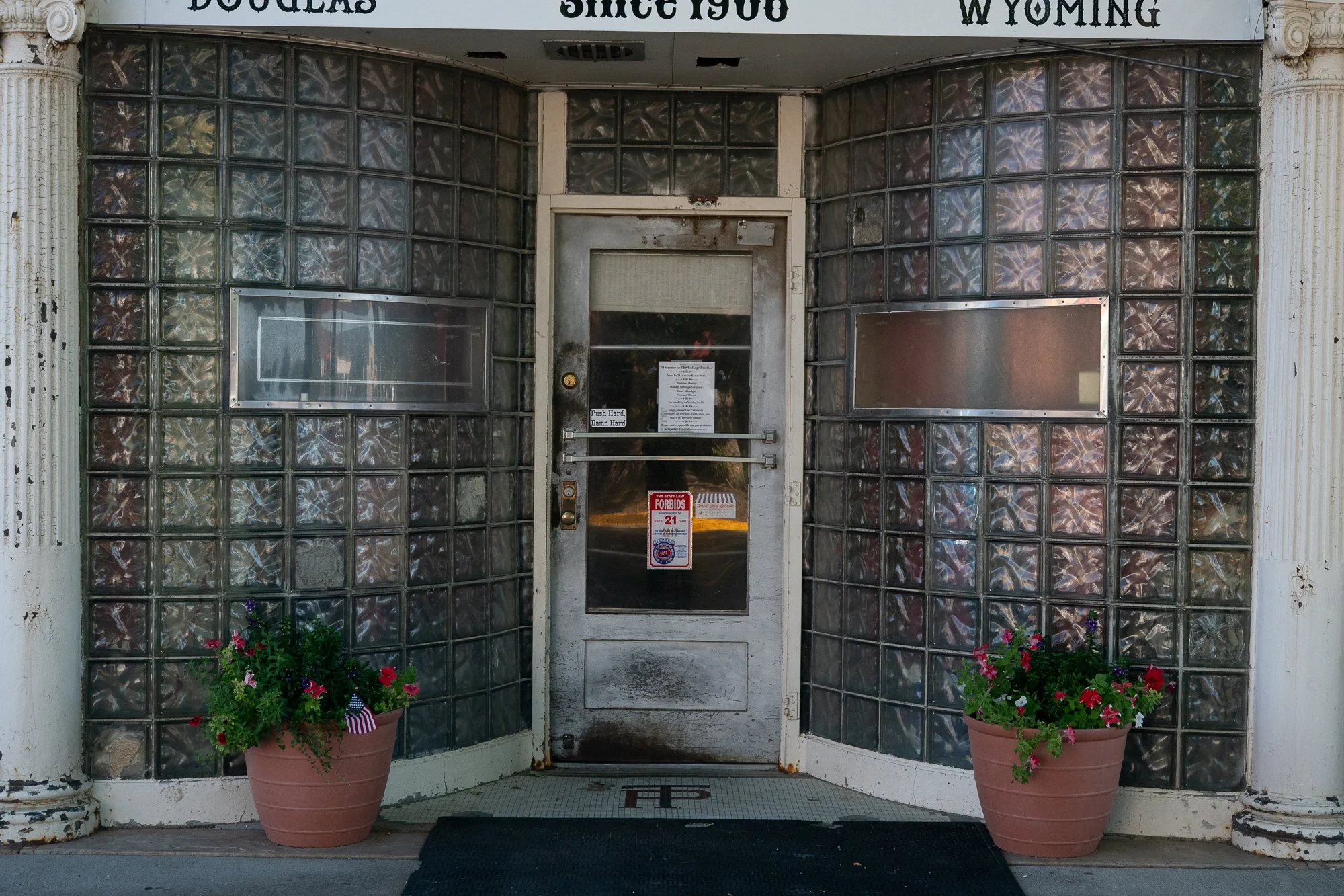Glass block entrance with a central door, decorative white columns and flower planters beneath a sign reading Douglas, Since 1908, Wyoming.