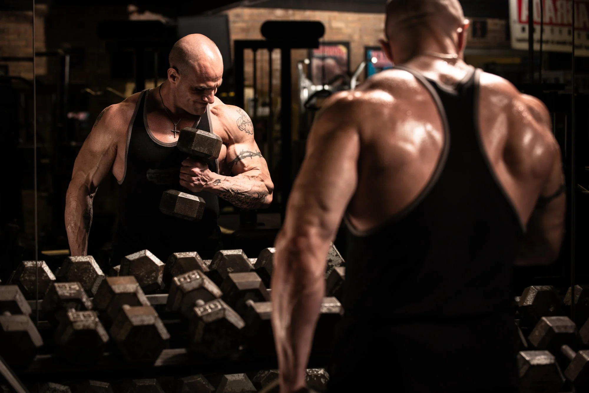 Muscular athlete lifting dumbbell in front of mirror gym workout