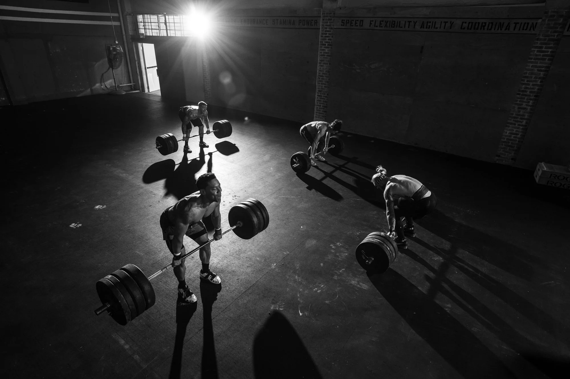 Four CrossFit athletes performing heavy barbell deadlifts in a gritty gym.