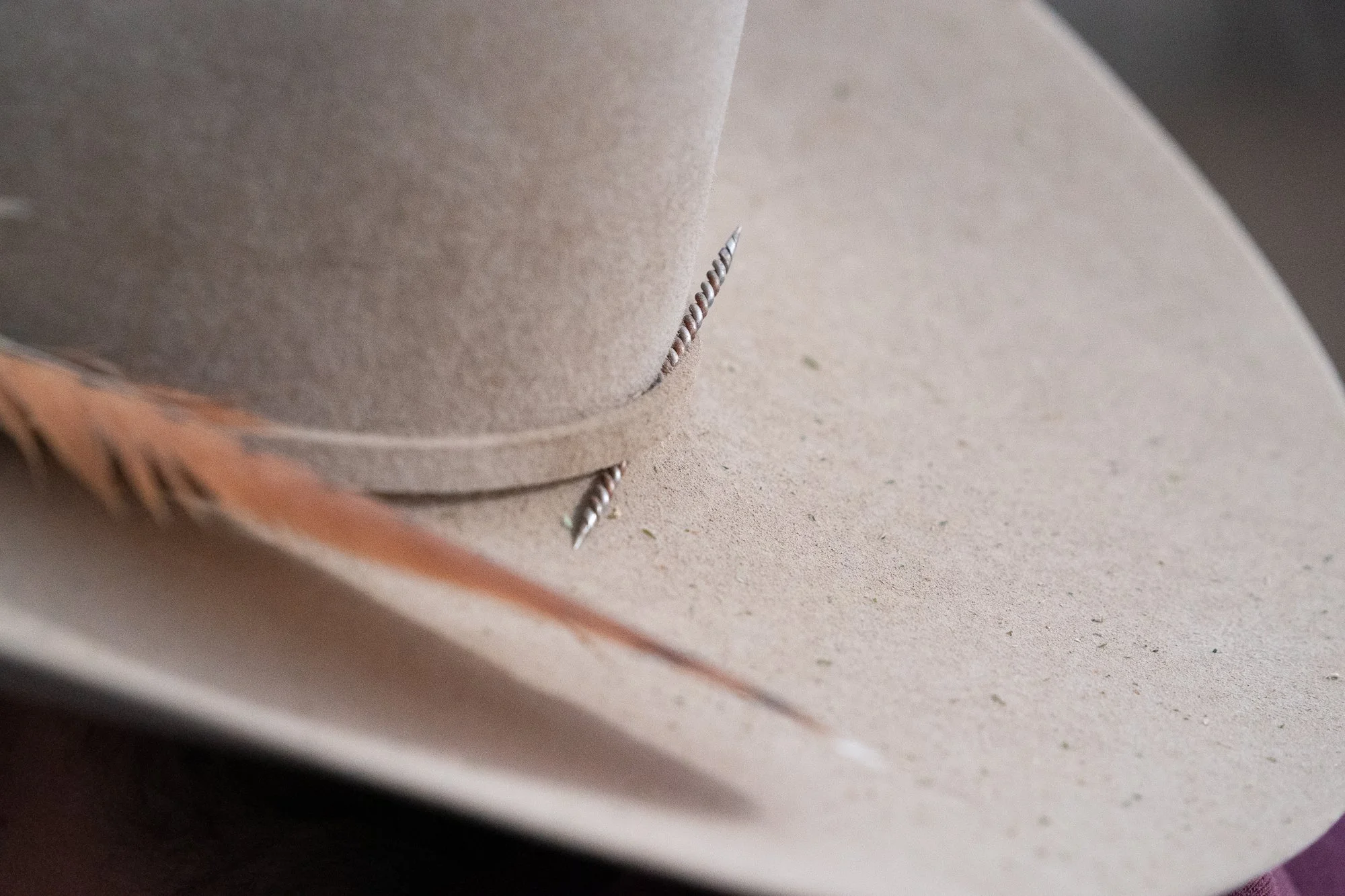 A close detail of a dusty cowboy hat with a small hat-band detail tucked into the band