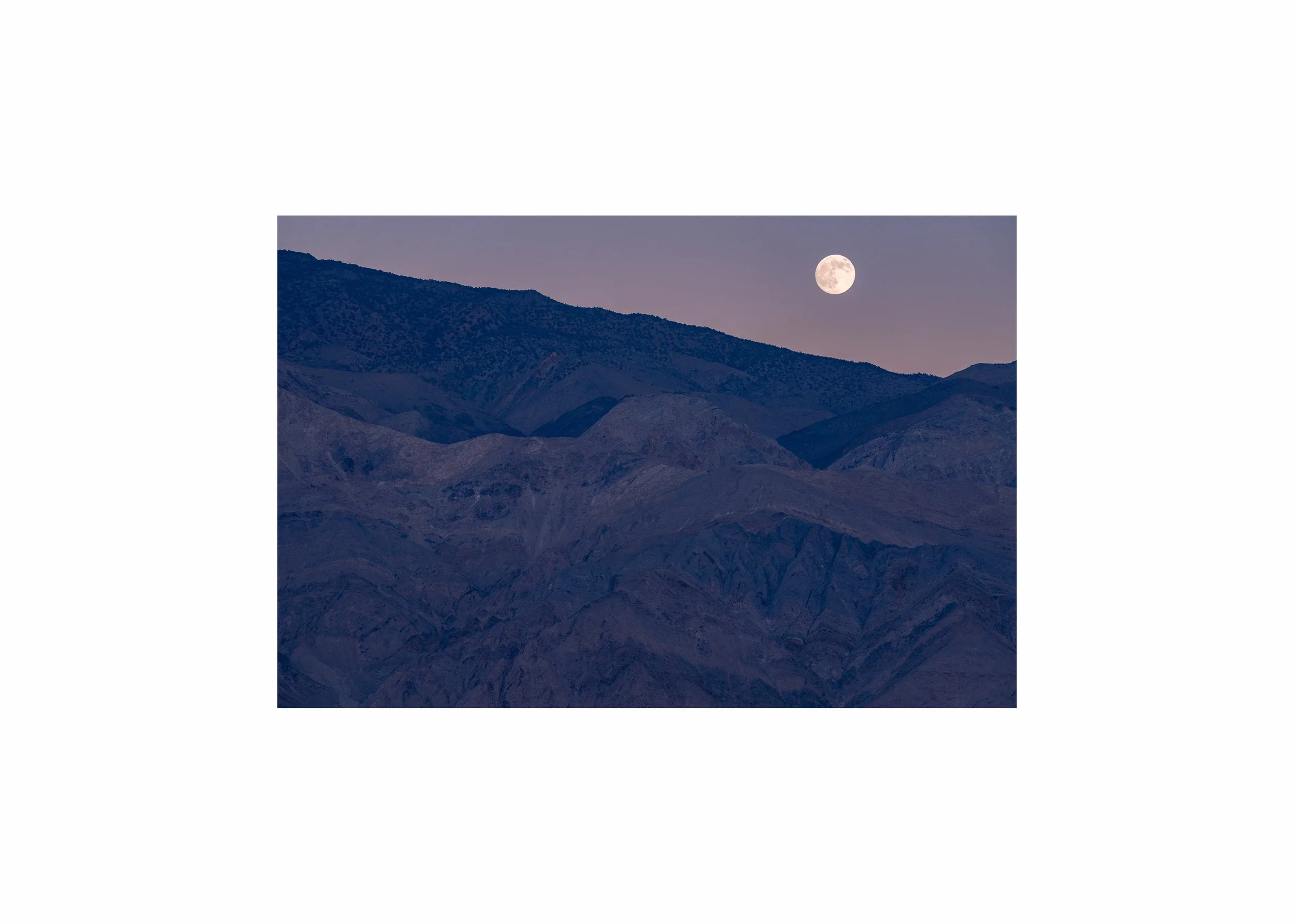 A large, bright moon over dark blue desert mountains at twilight.