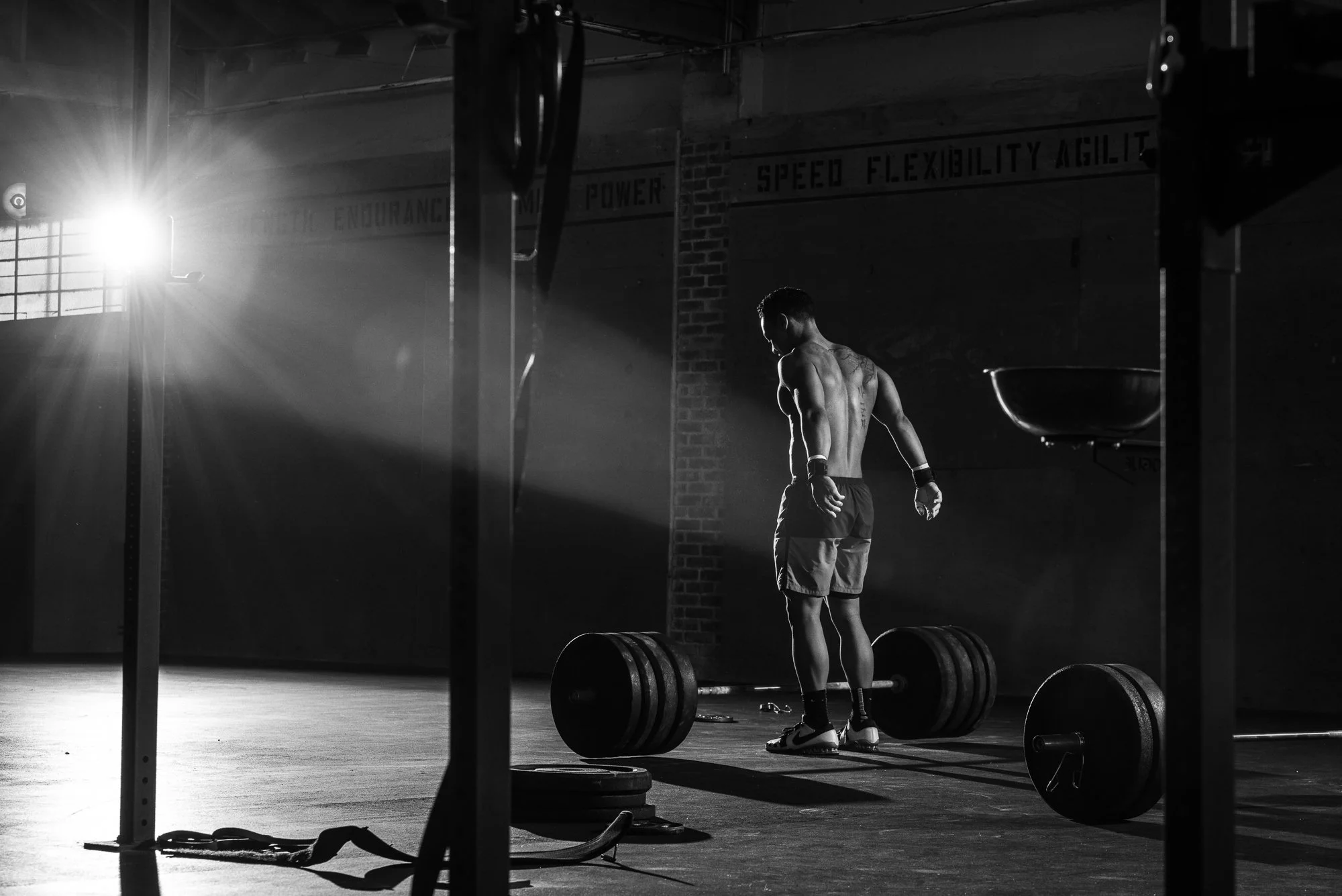 CrossFit athlete standing beside a loaded barbell as sunlight cuts across the gym floor.