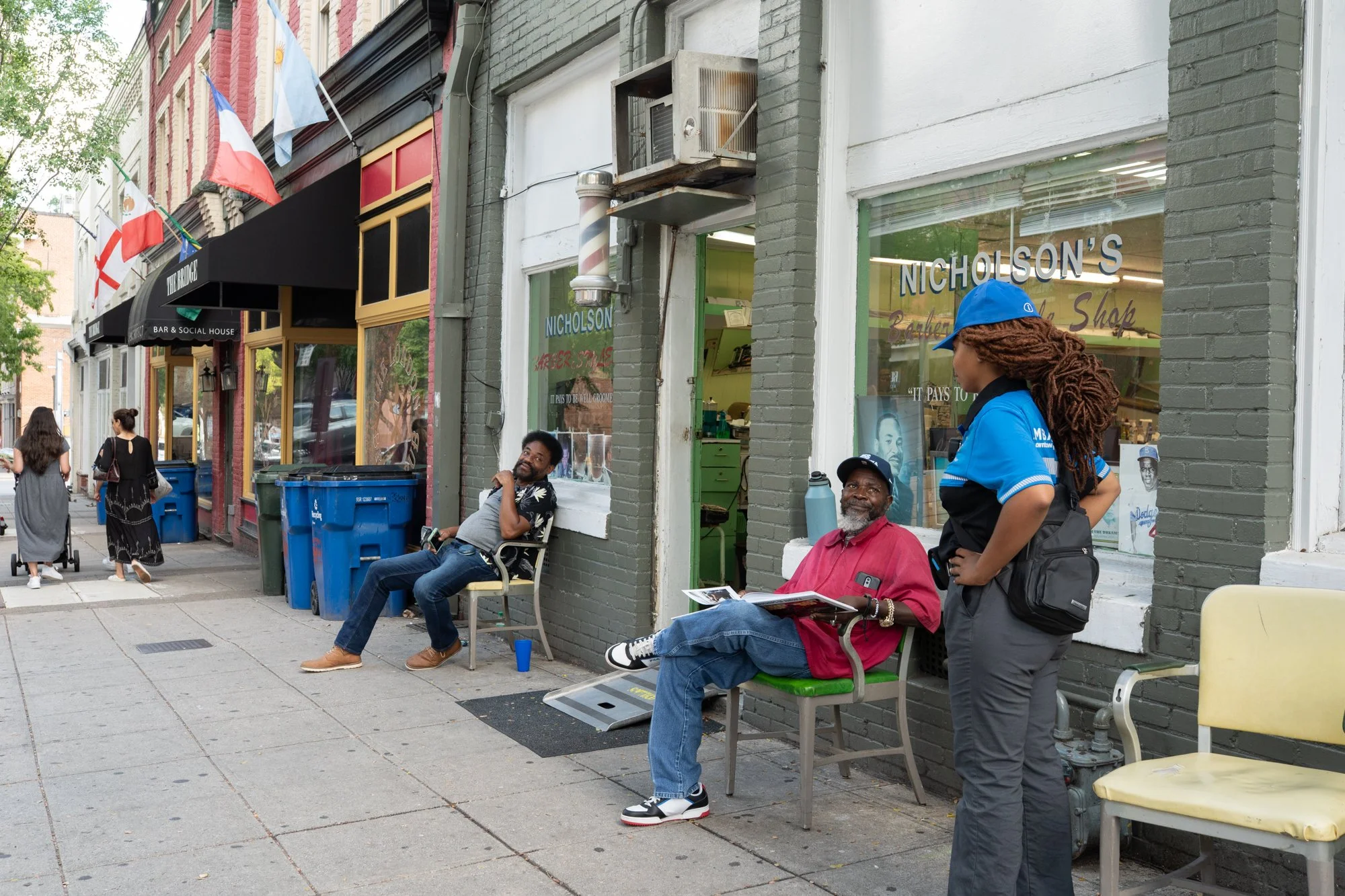 People sitting and talking outside a neighborhood barbershop on a city street
