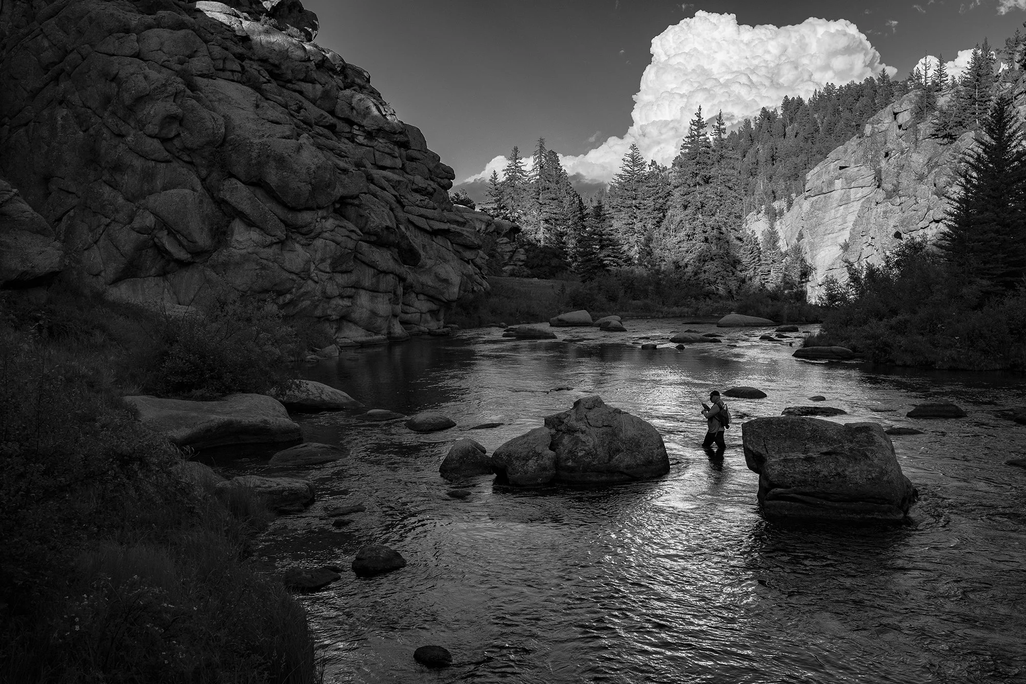 Black and white photograph of a fly fisherman on the South Platte River with dramatic storm clouds in the background