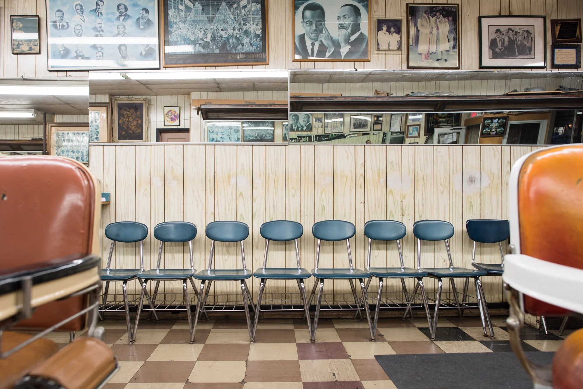 Row of empty chairs inside a historic Black barbershop with framed portraits and mirrors