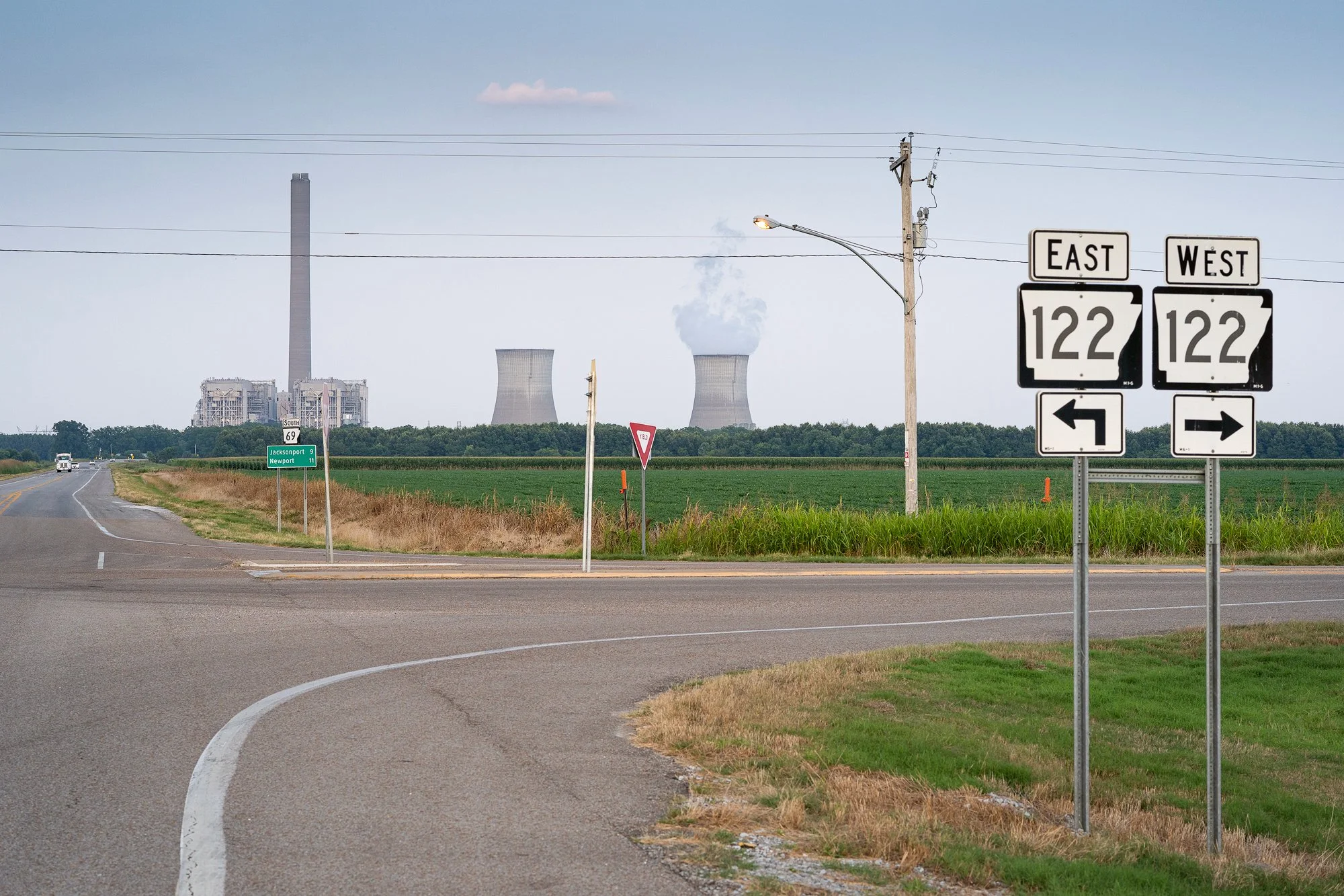 Rural highway intersection with directional signs and power plant in distance