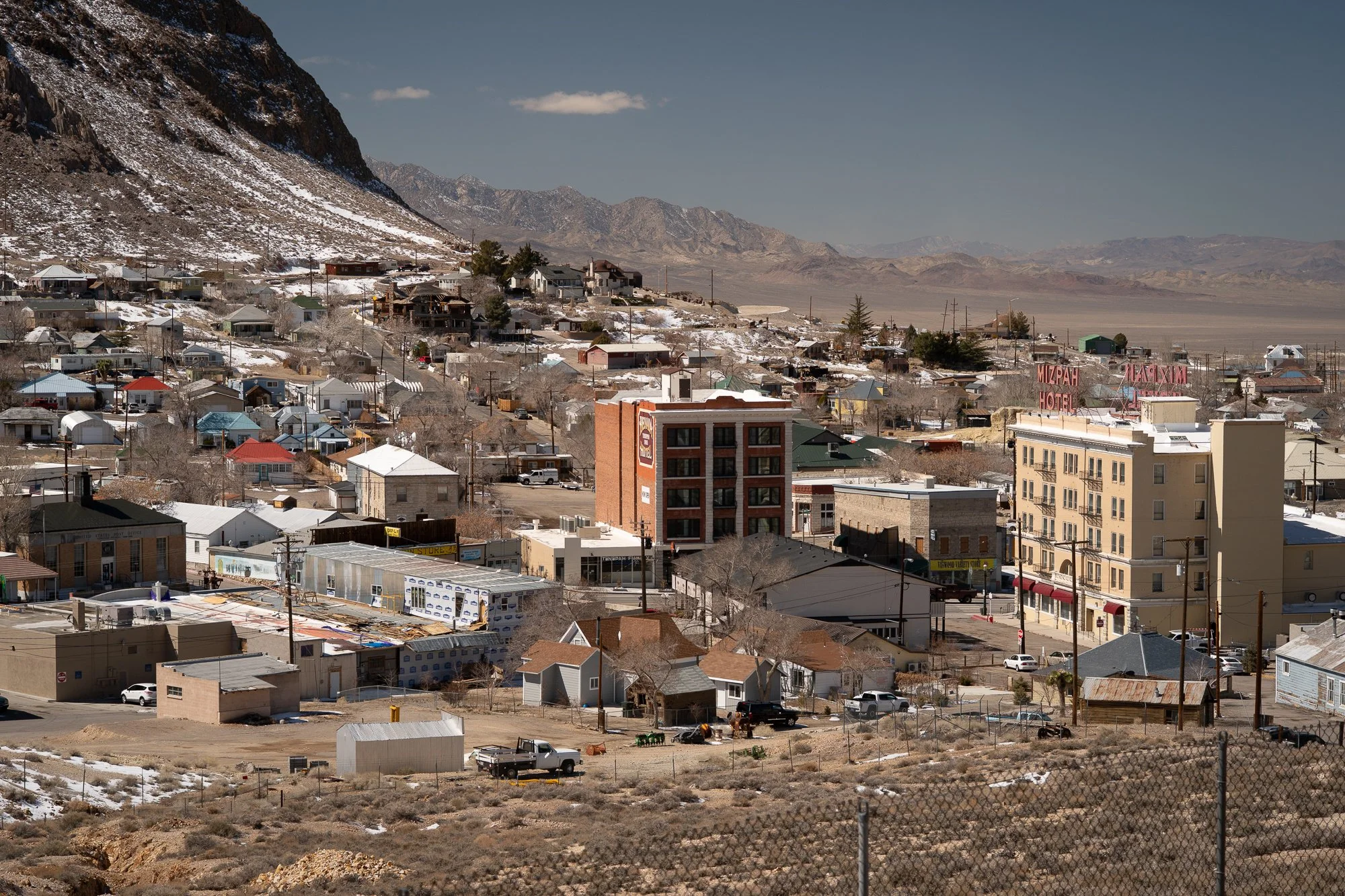 Elevated view of Tonopah, Nevada in winter with the Mizpah Hotel sign visible, residential homes climbing the hillside, and a wide desert basin and mountain range beyond.