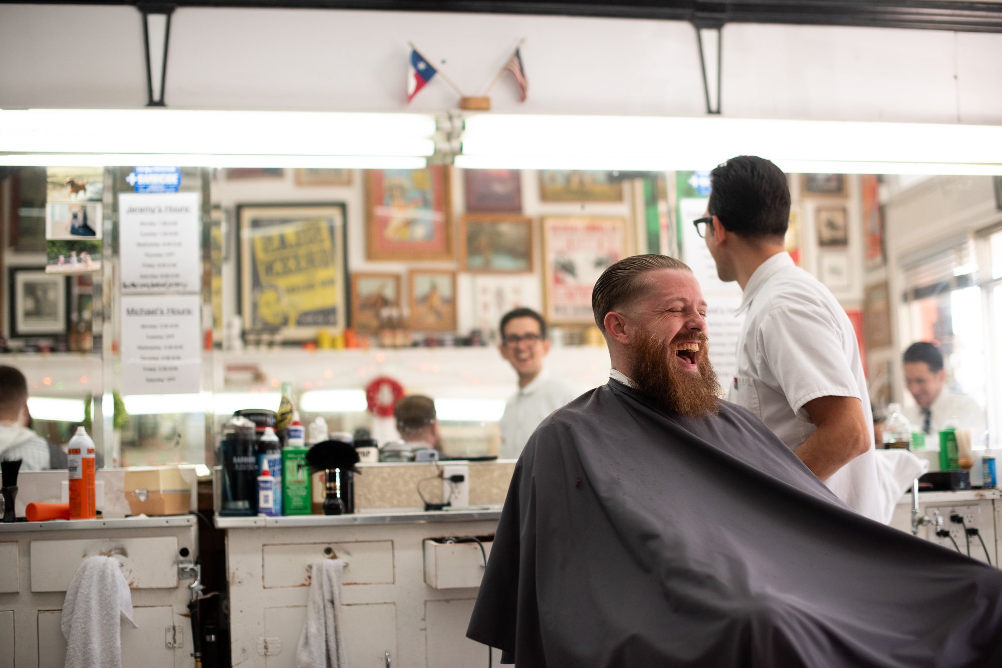 A man sits in a barber chair laughing inside Avenue Barbershop