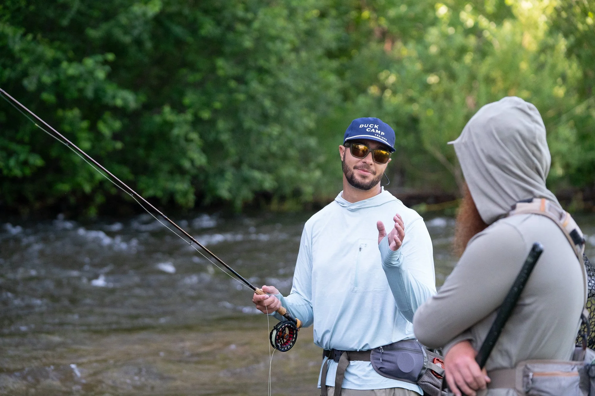 Two fly fishing anglers stand in the river while talking with rods and gear in hand