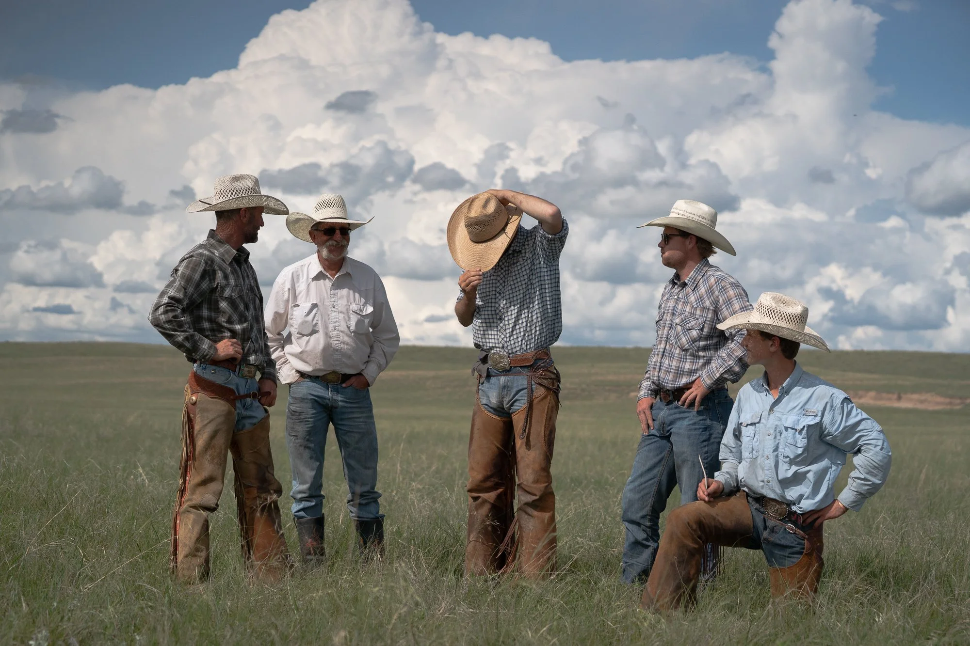 A group of working cowboys stand together in the Nebraska Sandhills at Haythorn Ranch beneath towering clouds.