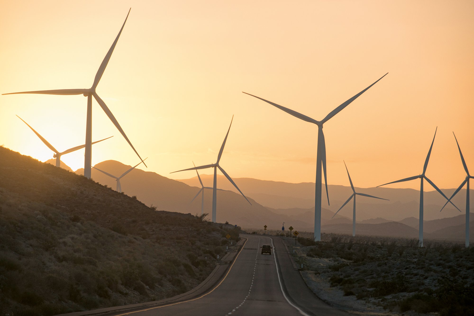 Wind turbines lining a desert road at sunset in the California landscape