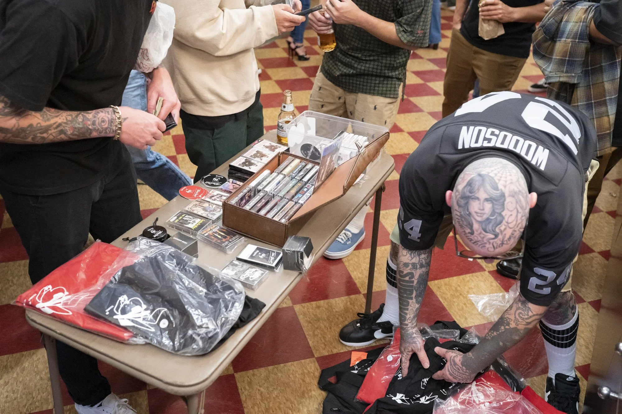 Merch table inside Syndicate Barbershop with cassette tapes, t-shirts, stickers, and branded items as attendees browse during the 20th anniversary celebration