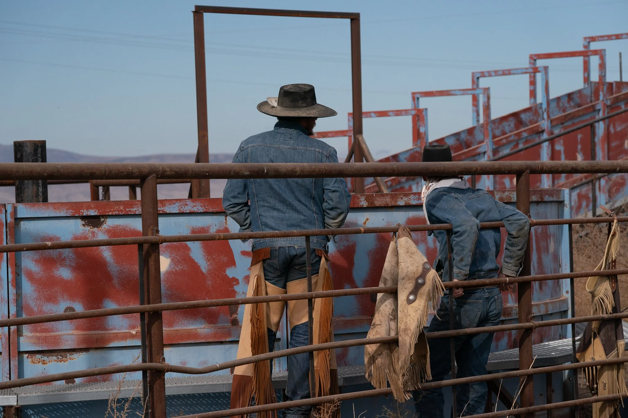 Two buckaroos standing at fence watching cattle work at TS Ranch