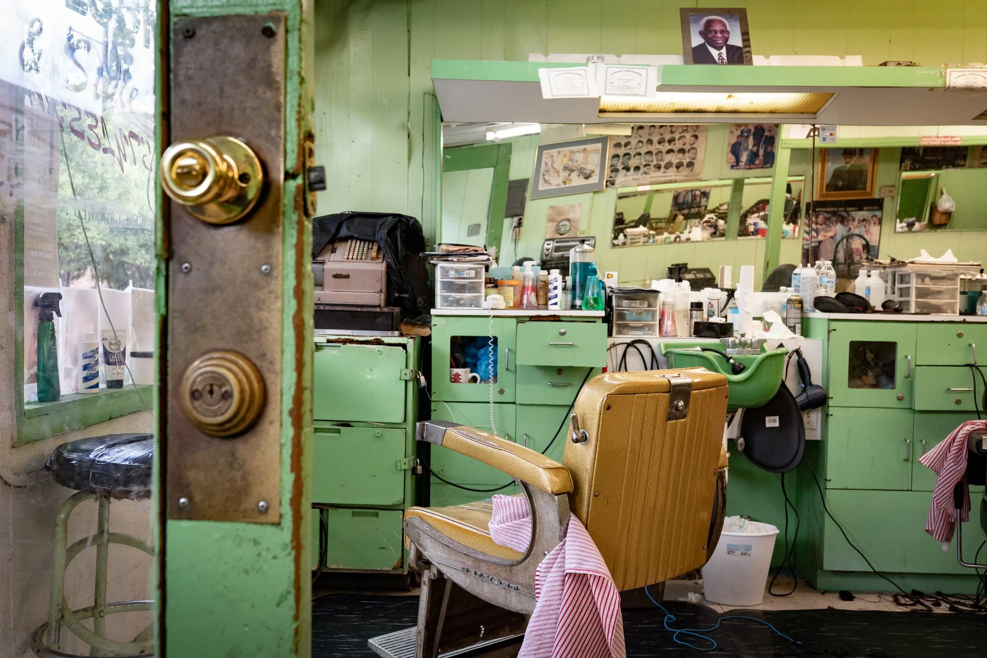 Interior of a barbershop with green cabinets and a vintage barber chair viewed through an open door