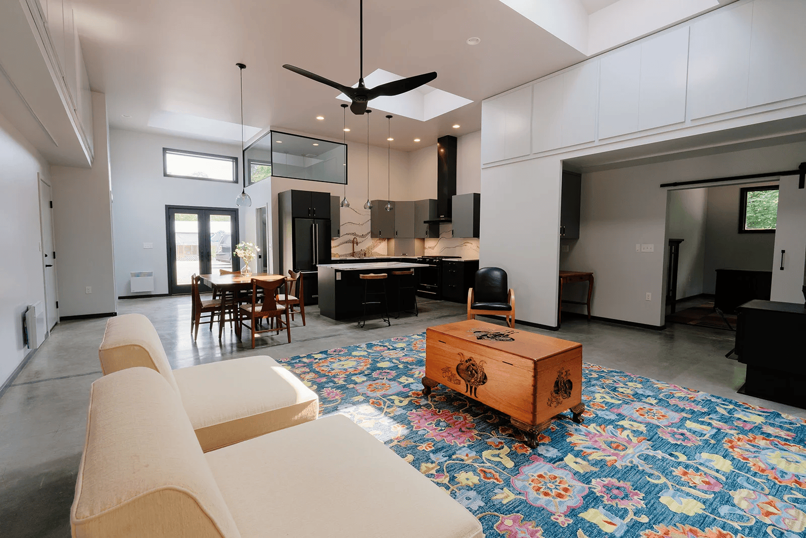 Open kitchen, dining, and living area with dark cabinetry and a colorful rug in the Vashon Hangar Home