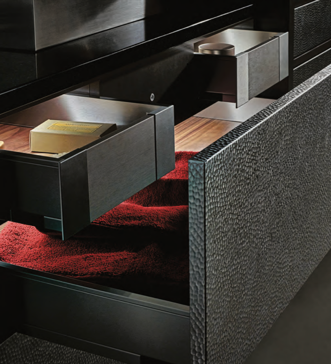 Close-up of a furniture piece with drawers open, revealing a red interior, a book, and small interior compartments, likely a modern cabinet or console table.