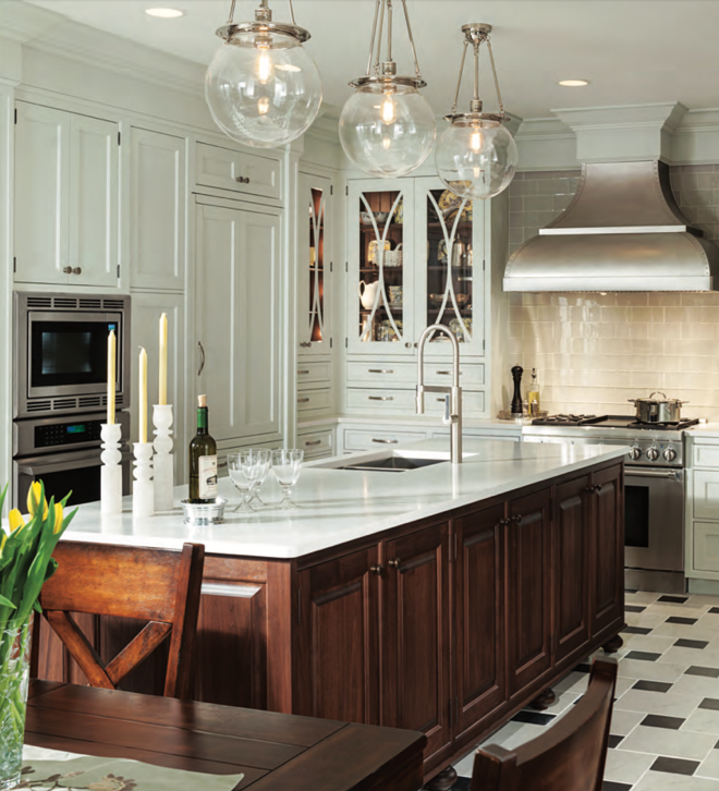 Modern kitchen with white cabinetry, stainless steel range hood, and dark wooden island, decorated with glass pendant lights and candle holders on the island.