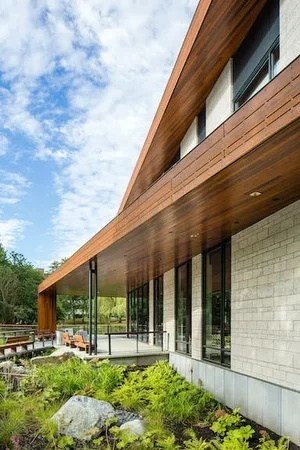 Modern building with wooden overhang, large glass windows, and landscaped garden with rocks and greenery.