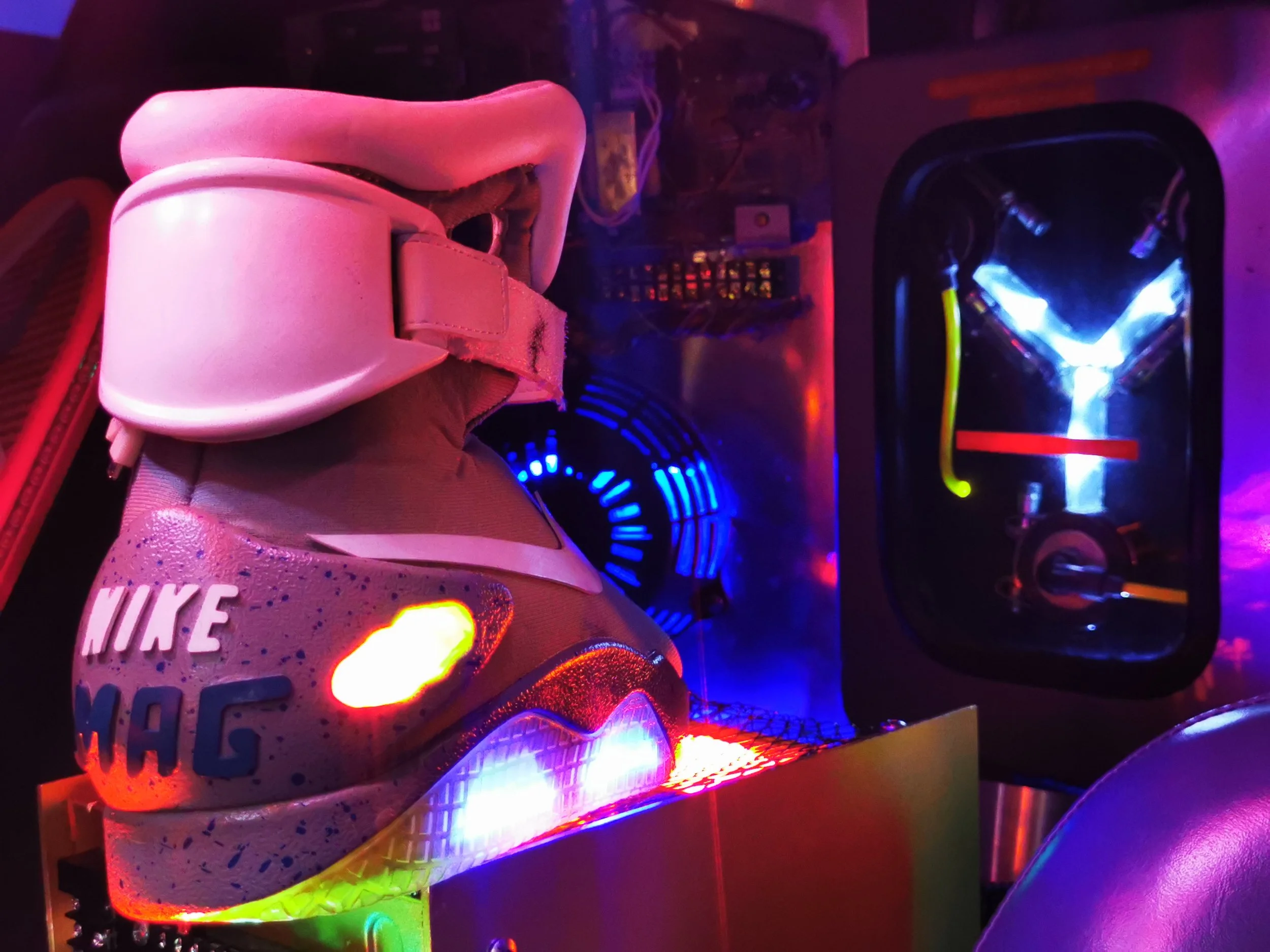 Close-up of a pink Nike sneaker with colorful glowing lights and a textured sole, placed next to a fluorescent light source, in a dimly lit environment.